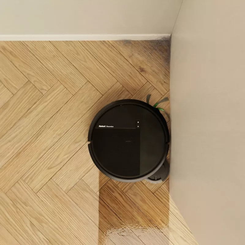 Czarny robot sprzątający czyści drewnianą podłogę w jodełkę.