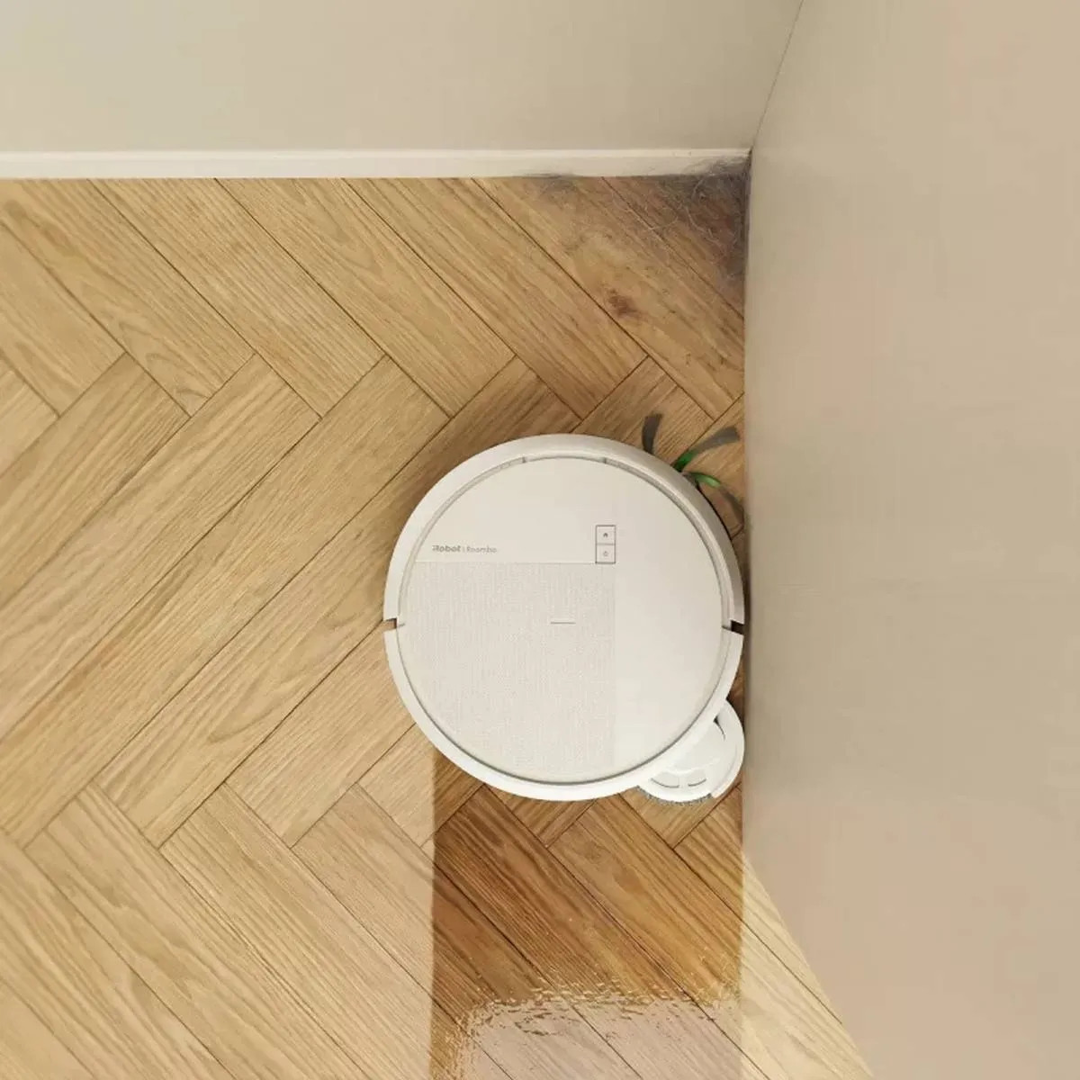 Biały robot sprzątający czyści drewnianą podłogę w jodełkę w rogu.
