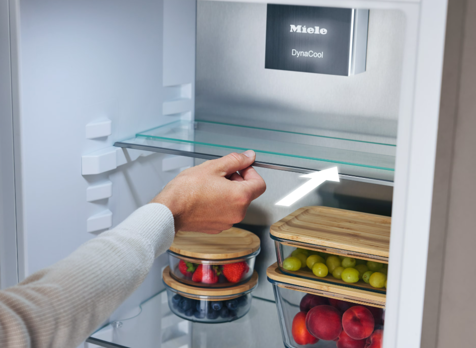 Hand schiebt ein Glasregal in einen Miele Kühlschrank mit Obst.
