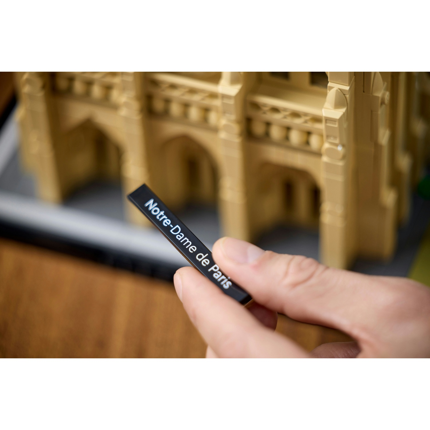 Una mano tiene una targhetta nera 'Notre-Dame de Paris' davanti a un modello Lego.