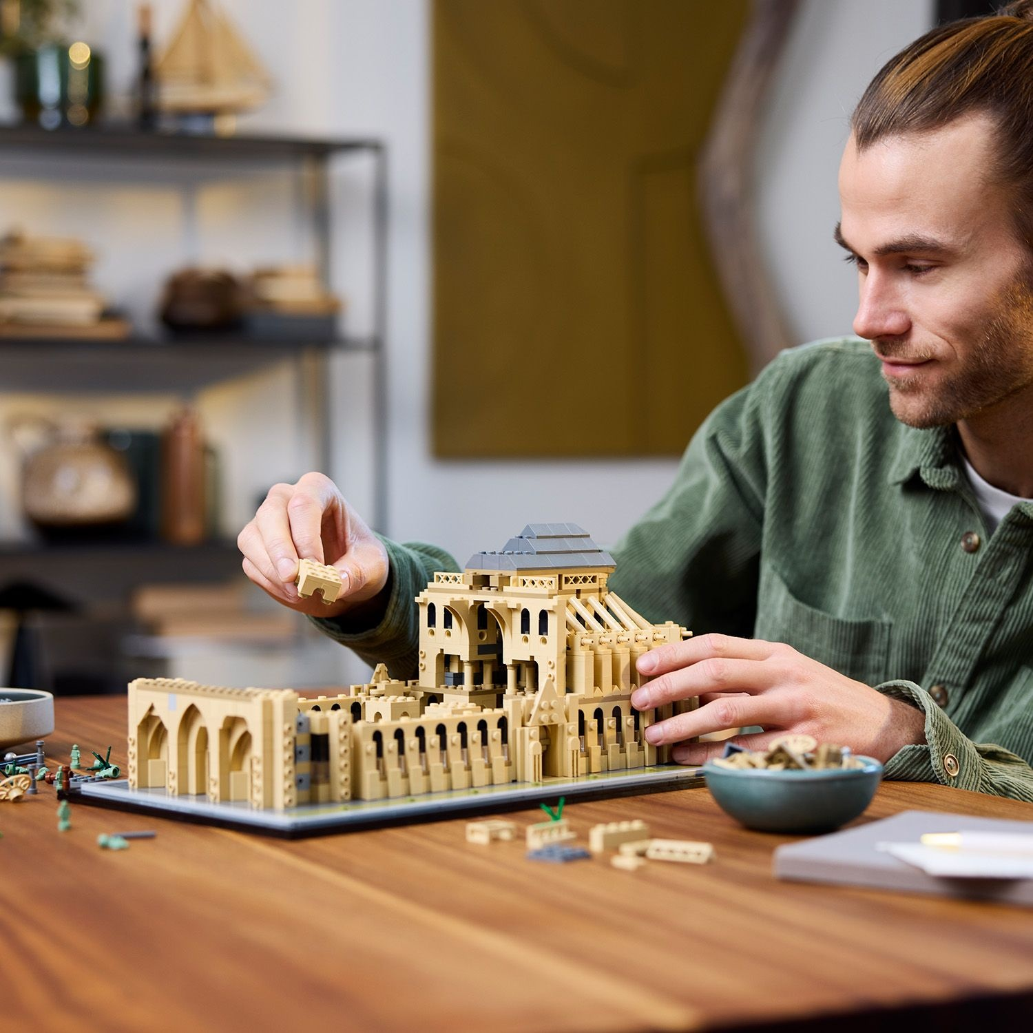 Uomo che costruisce un modello Lego beige di Notre Dame su un tavolo di legno.