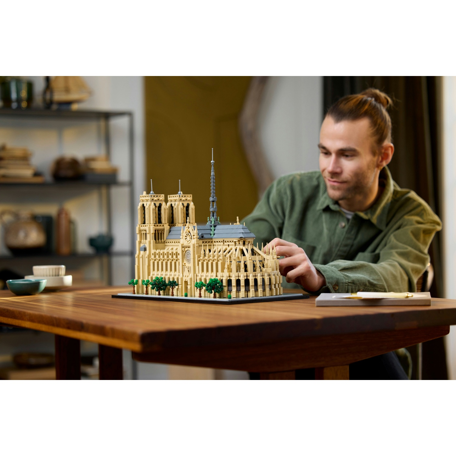 Un uomo costruisce un modello Lego color sabbia di Notre Dame su un tavolo di legno.