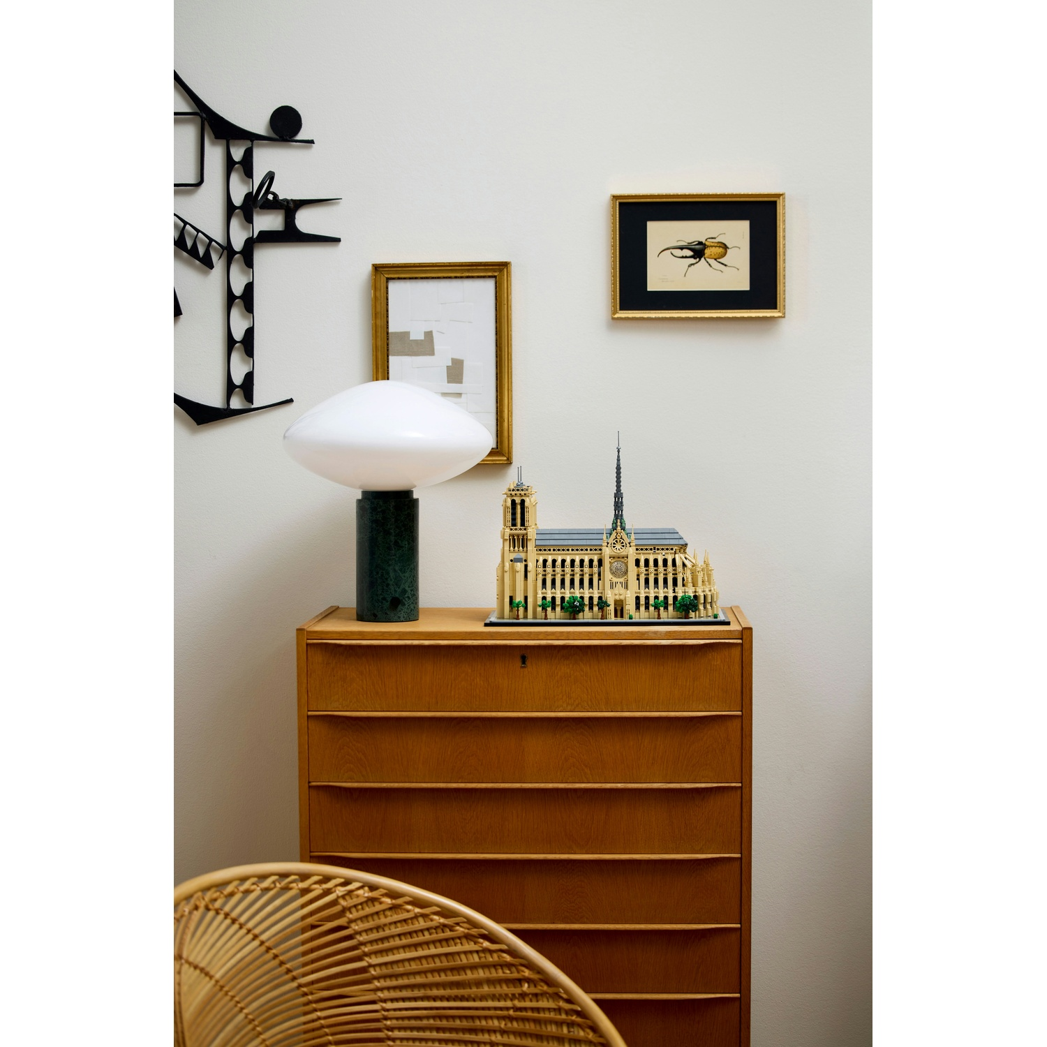 Cassettiera in legno con modello Lego di Notre Dame, lampada e quadro di coleottero.