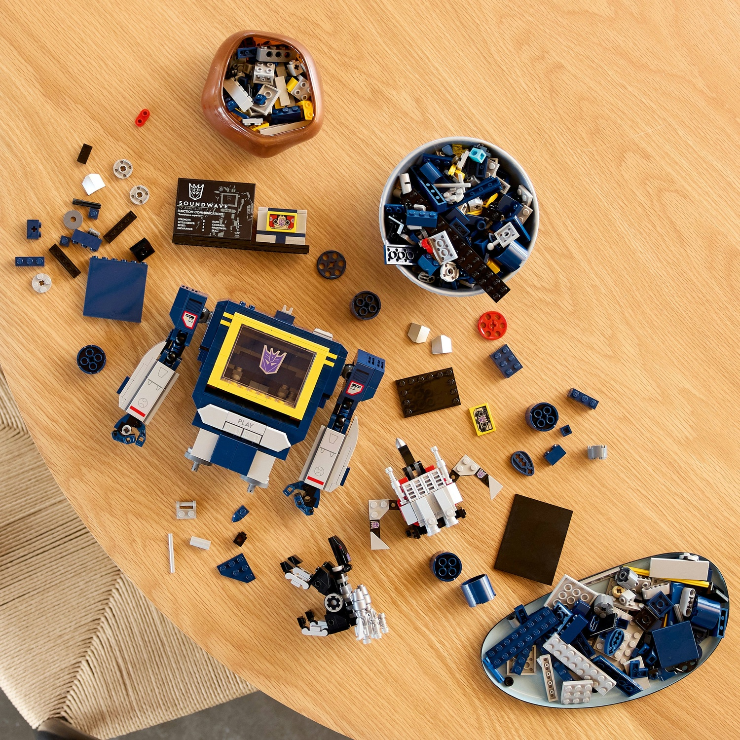 LEGO "Soundwave" e figure più piccole su tavolo di legno, con blocchi sparsi.