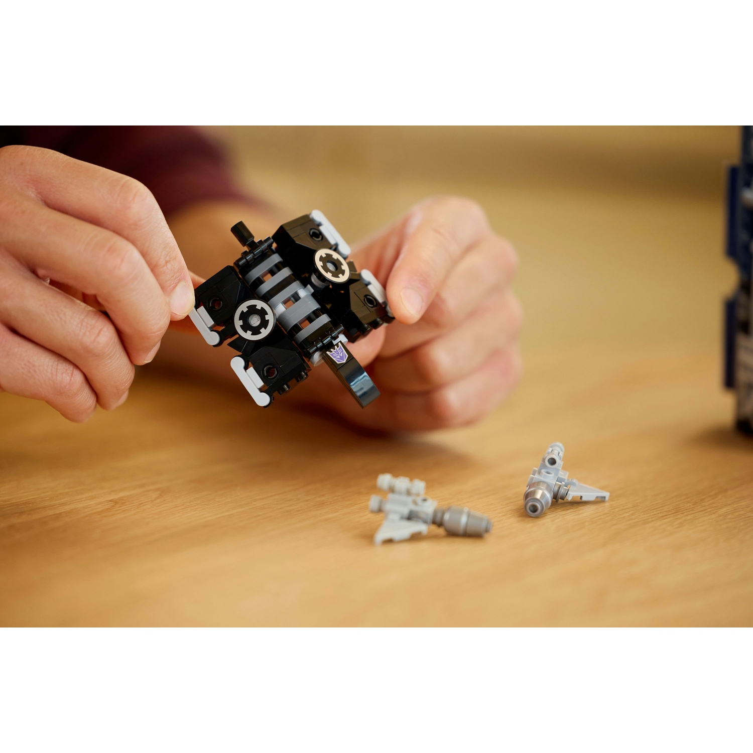 Mani assemblano un oggetto Lego nero e grigio con piccole armi grigie accanto.