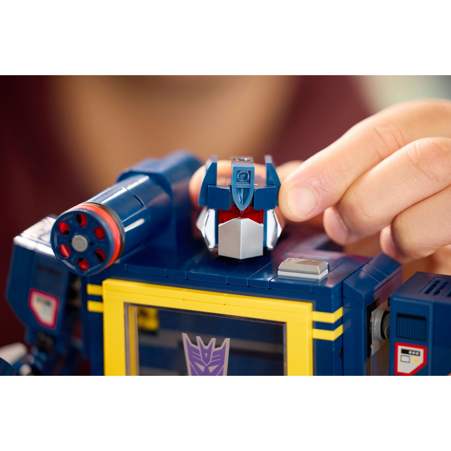 Un giocattolo Transformer blu Lego con accenti gialli. Una mano ne regola la testa.