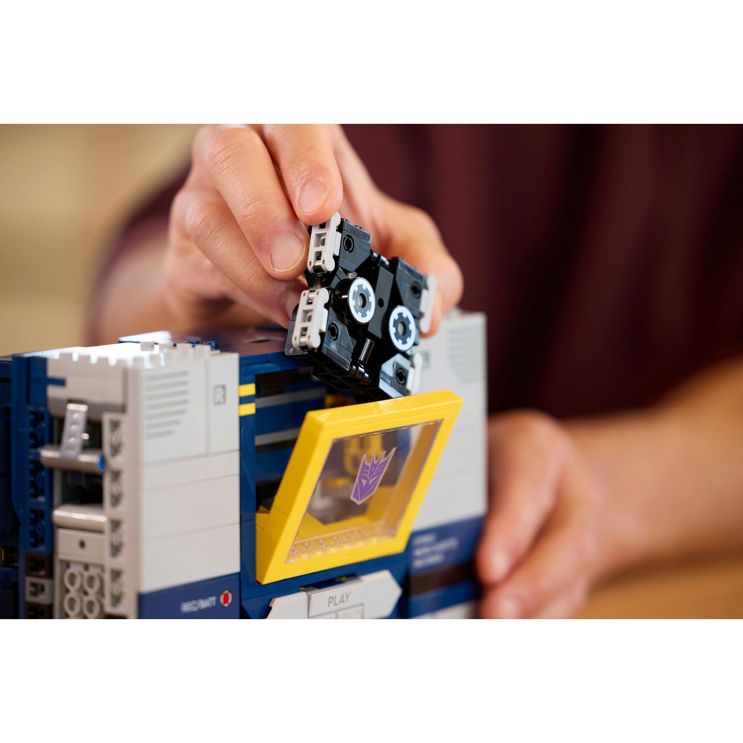 Una mano inserisce una musicassetta in un dispositivo Lego blu e grigio.