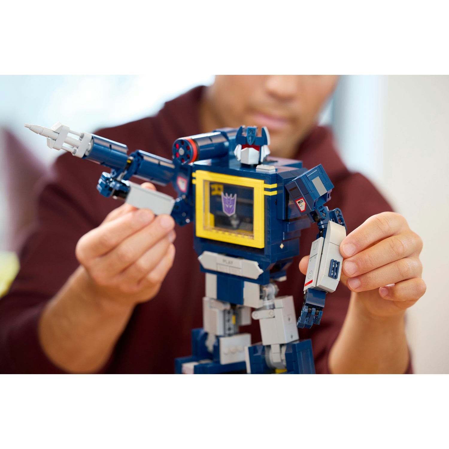Un uomo tiene una figura Lego blu e grigia con una finestra gialla.