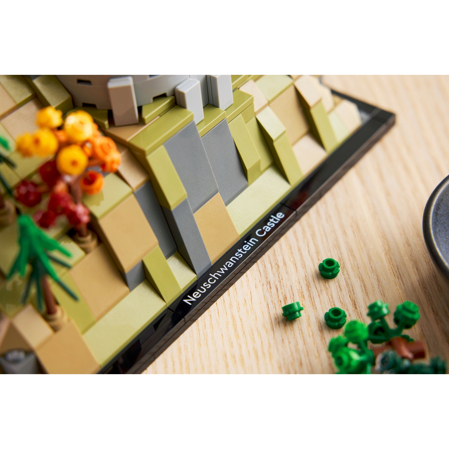 Modello Lego Castello Neuschwanstein con alberi verdi e fiori arancioni su legno.