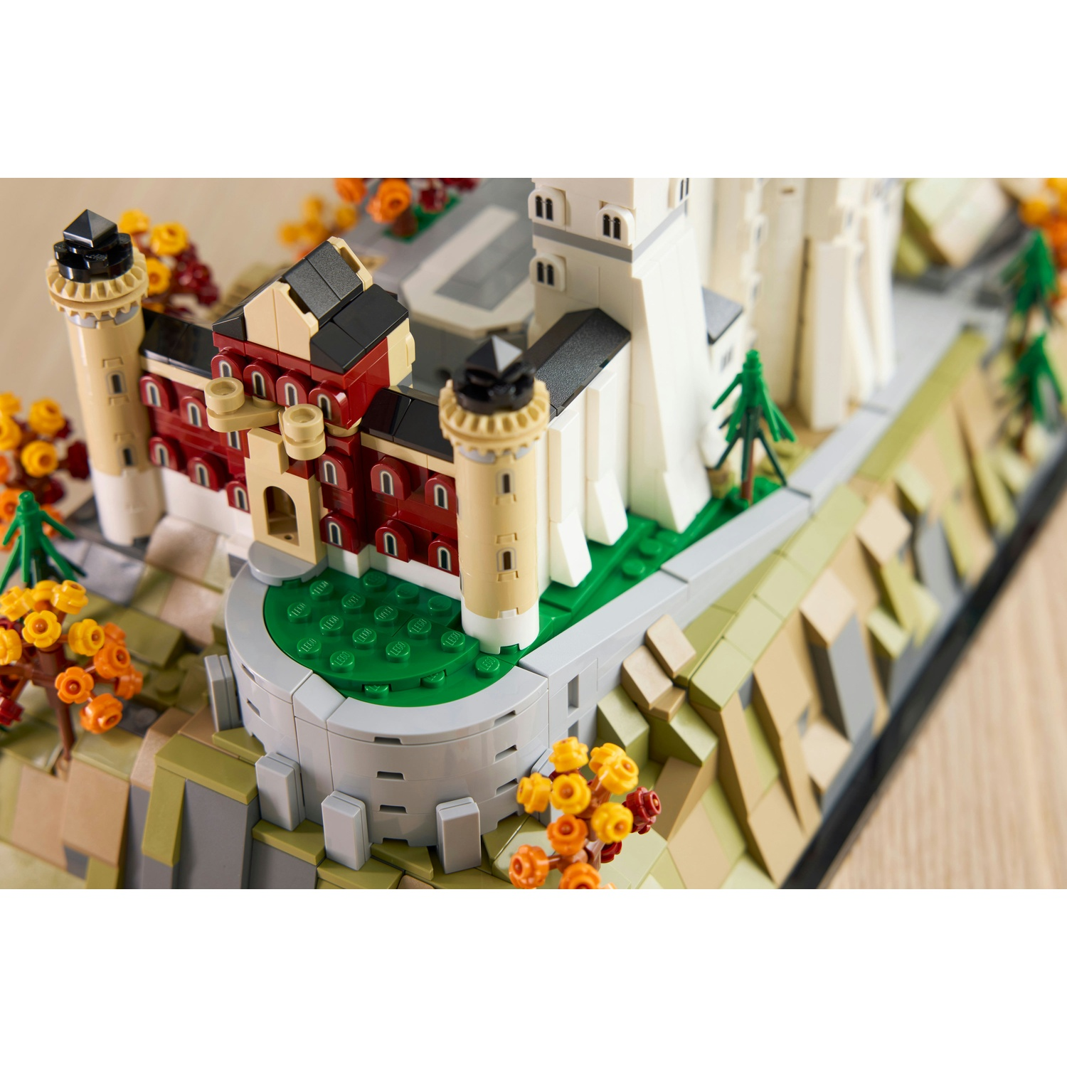Modello Lego di un castello con torri rosse e bianche, circondato da fogliame e alberi autunnali.