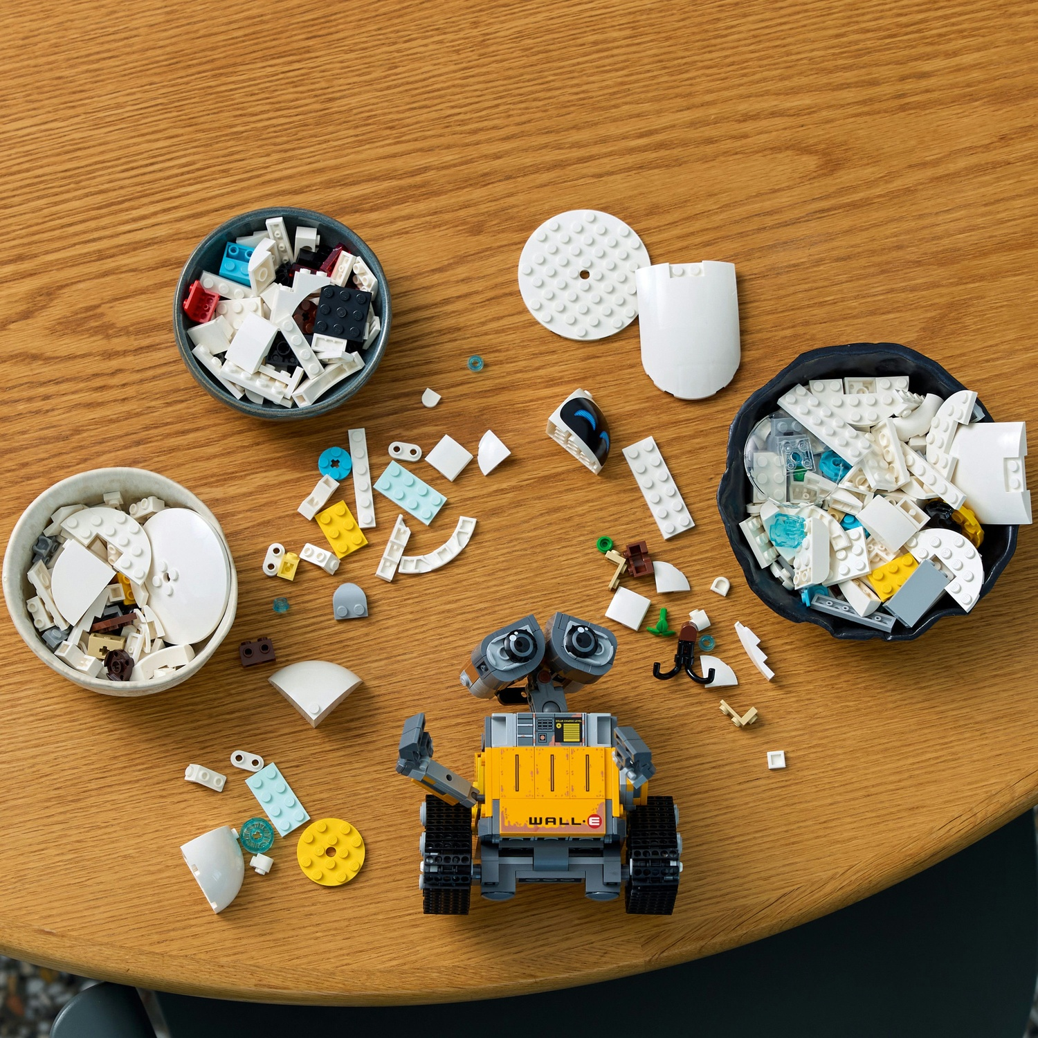 Un modello LEGO di WALL-E è su un tavolo di legno circondato da mattoncini sparsi e ciotole di pezzi.