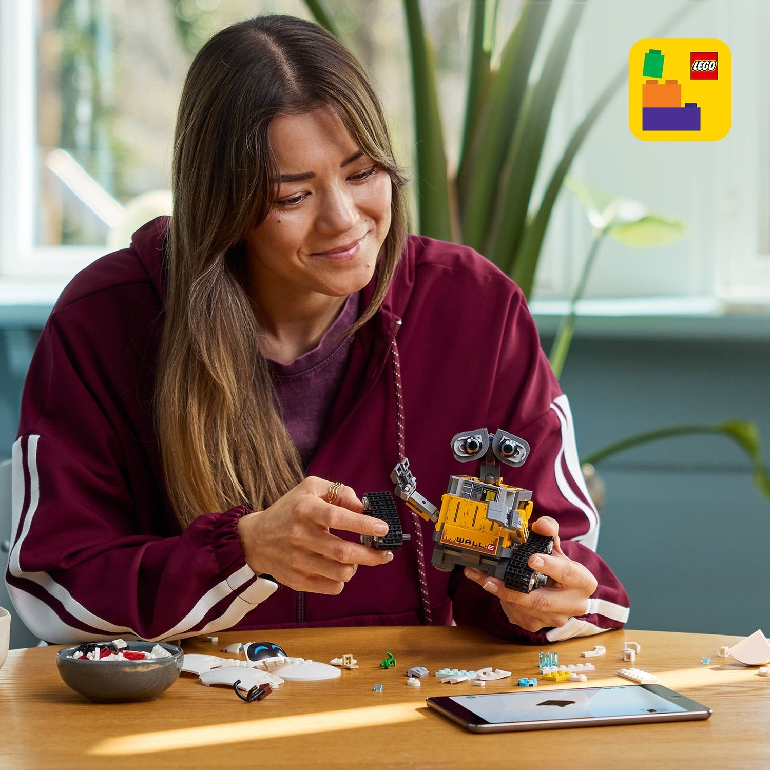 Donna costruisce Lego WALL-E su tavolo di legno, con tablet e mattoncini.
