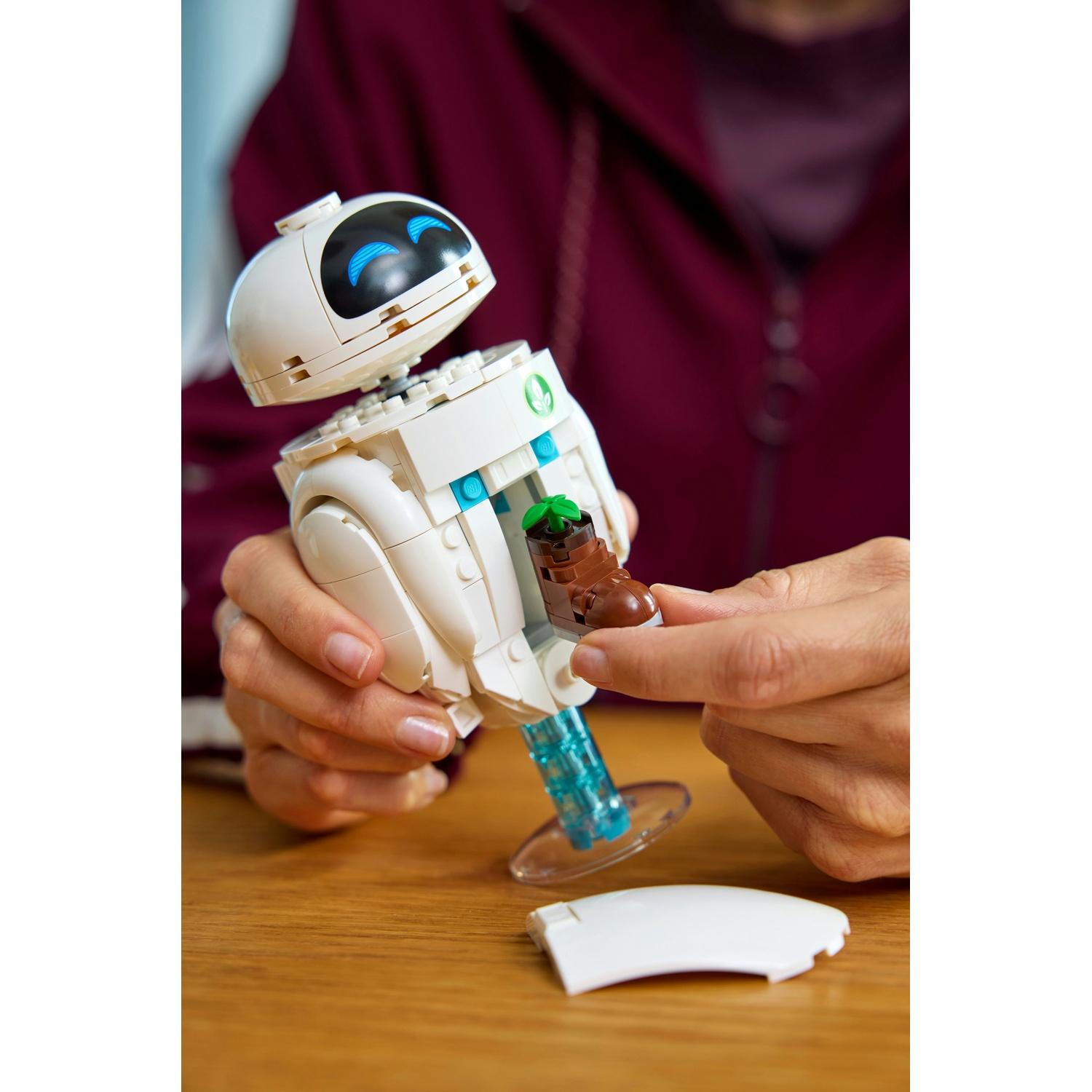 Robot Lego bianco con occhi blu, mani inseriscono parte di pianta.