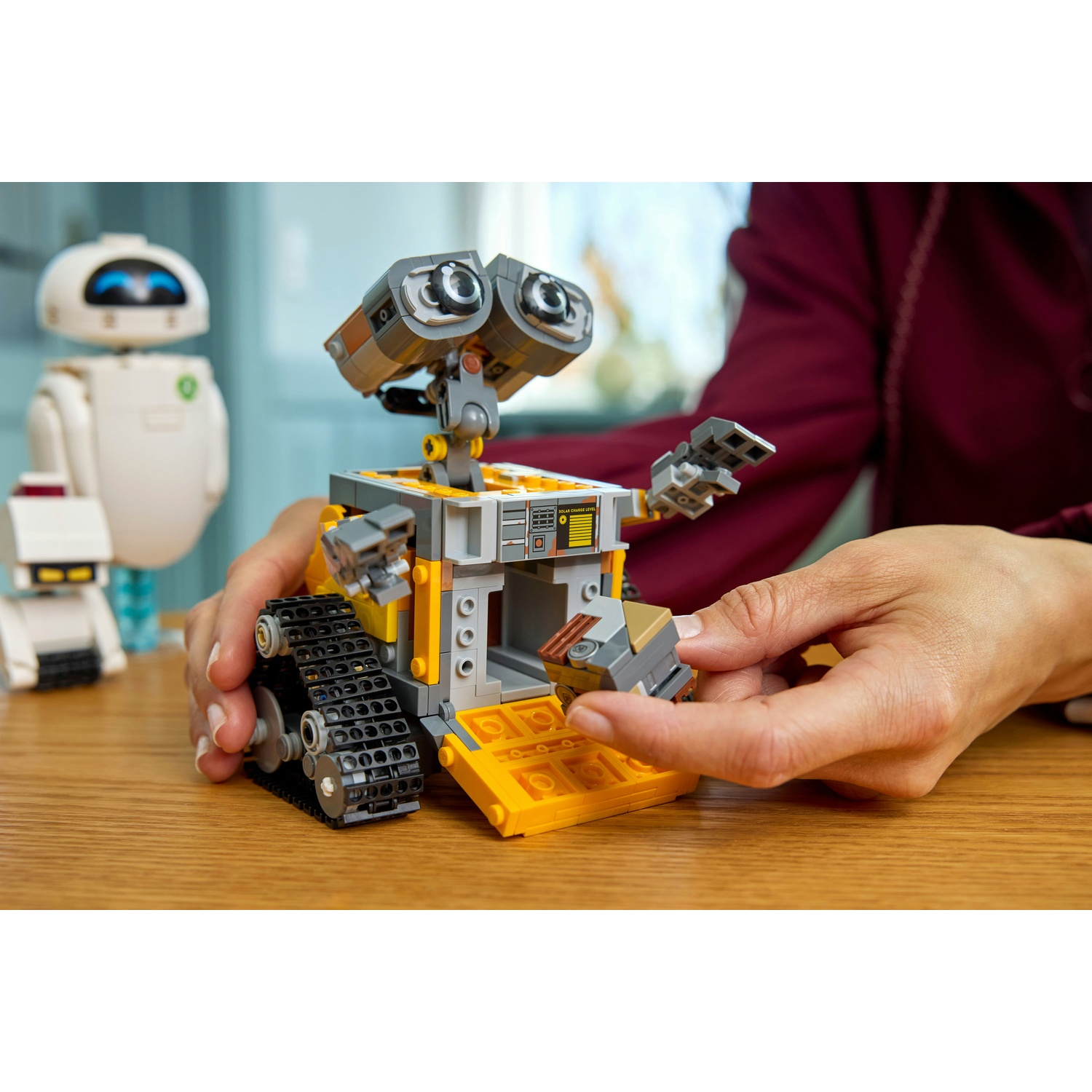 Un modello Lego di Wall-E viene costruito da mani su un tavolo di legno.