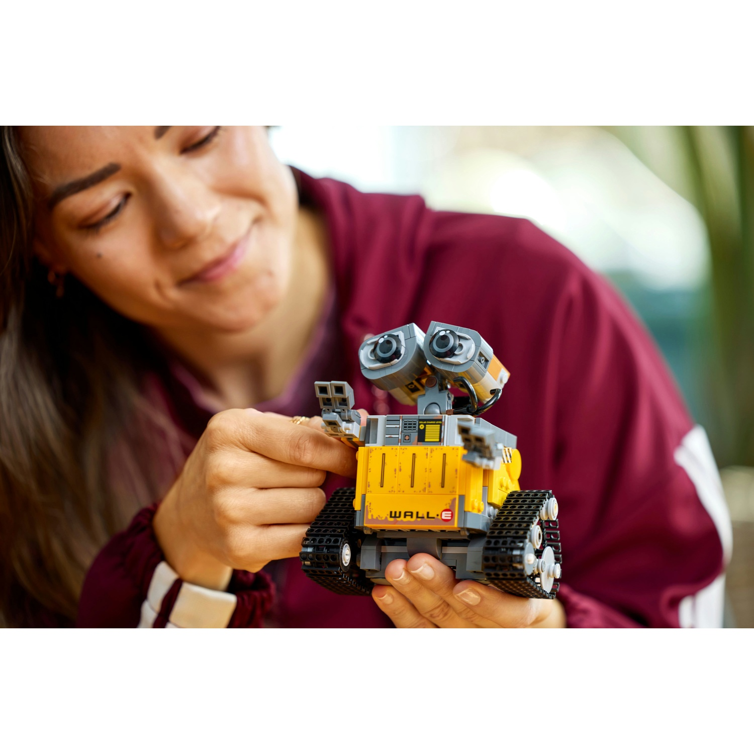 Una donna tiene un robot LEGO WALL-E giallo con cingoli.