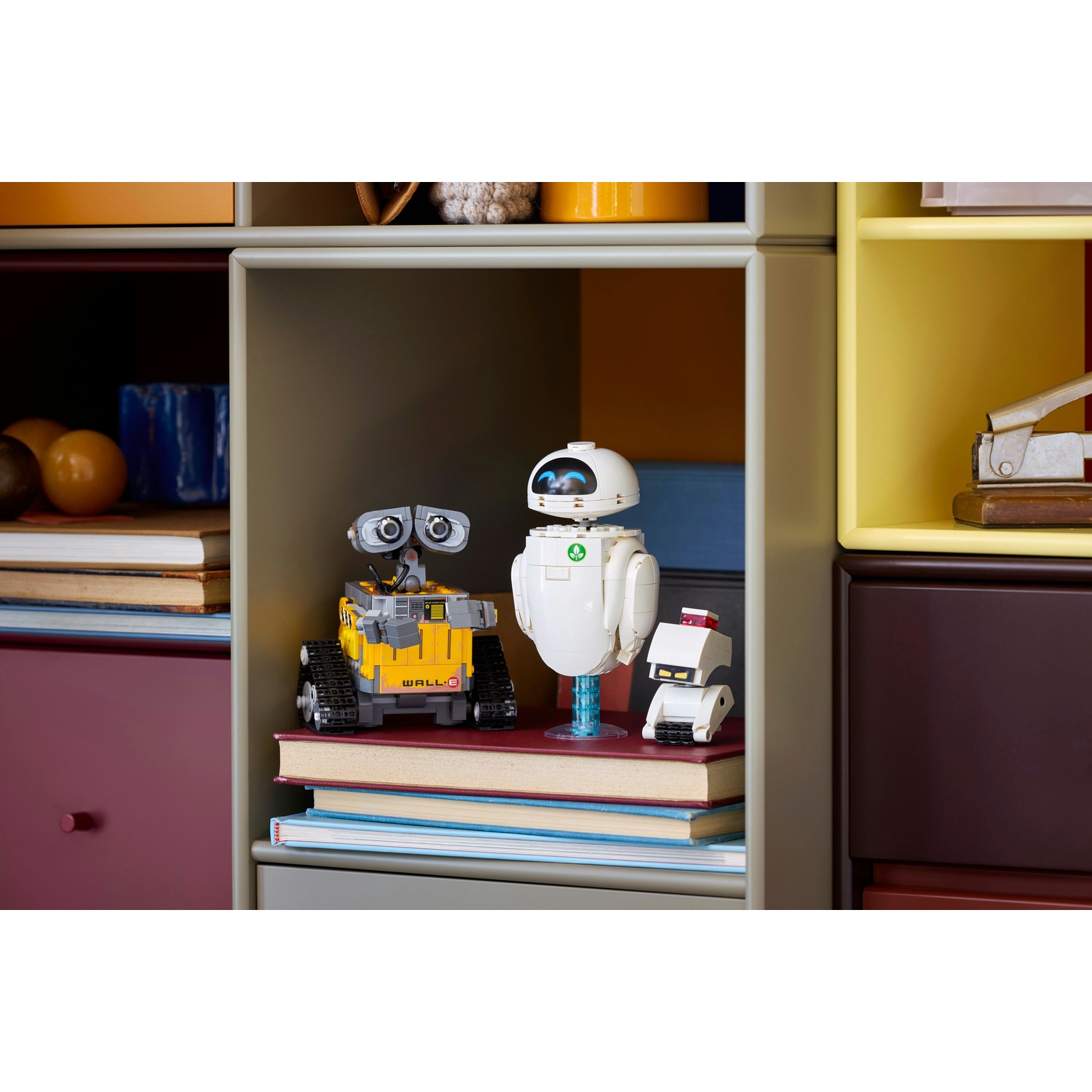 Tre robot giocattolo, tra cui WALL-E, stanno sui libri in una mensola.