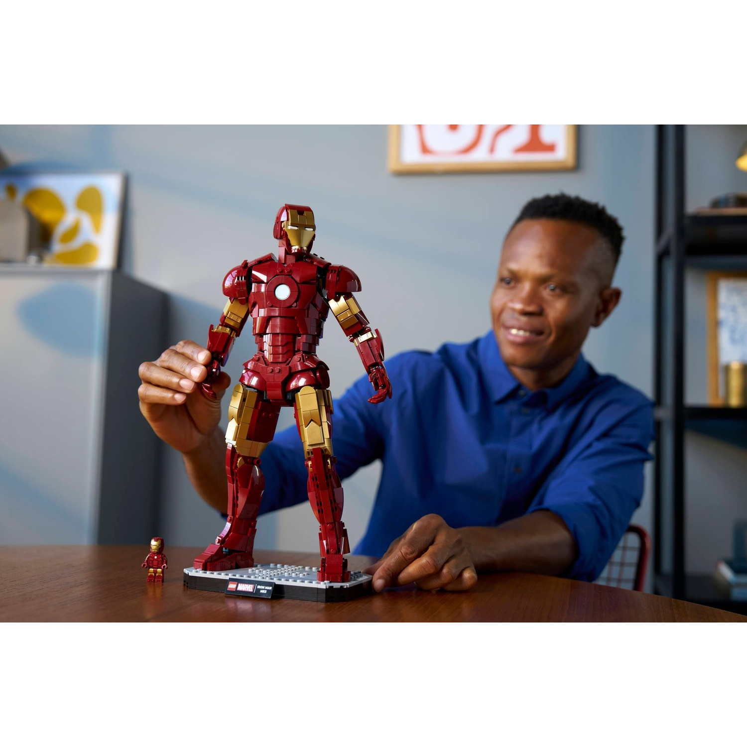 Uomo in camicia blu sistema una grande figura Lego di Iron Man accanto a una piccola.