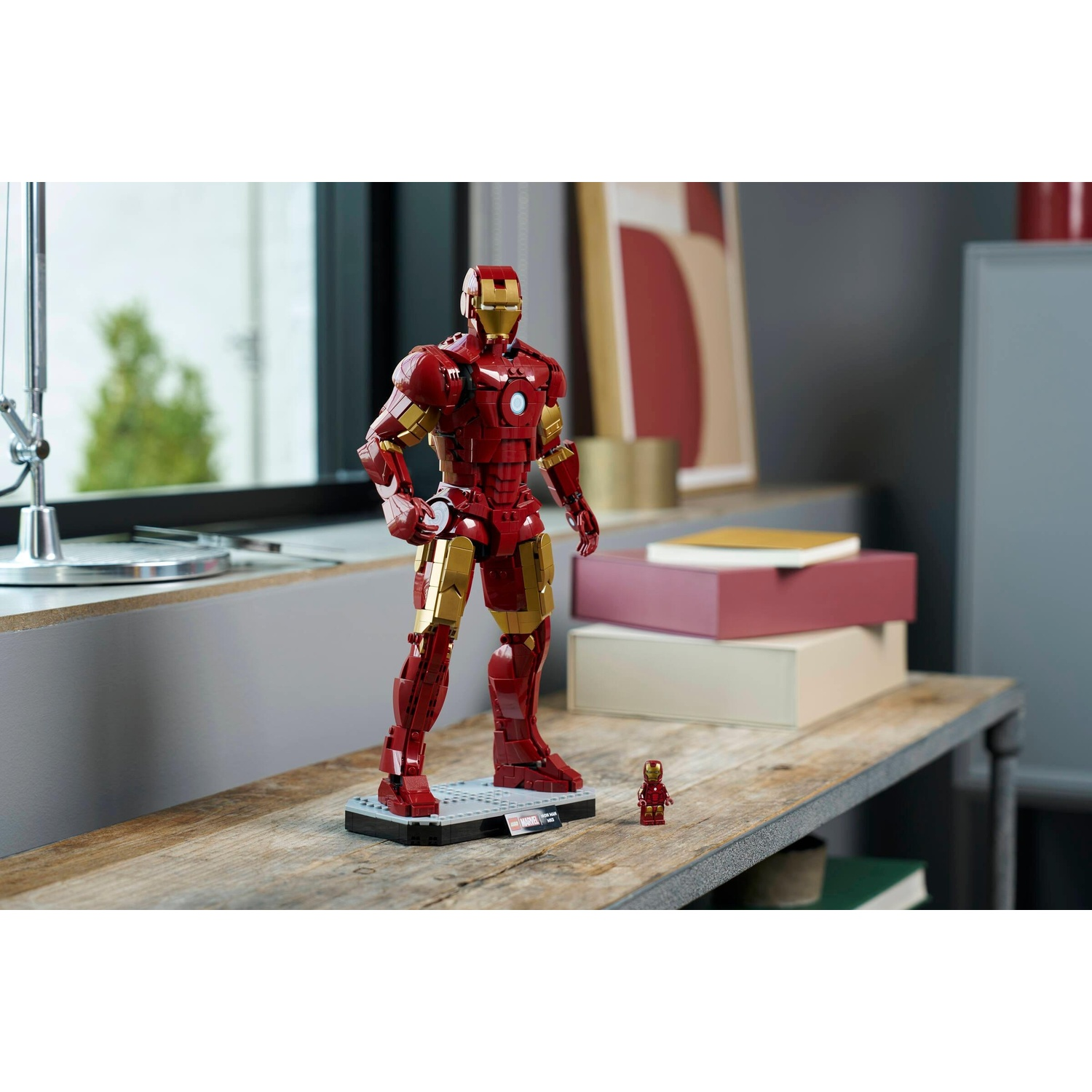 Un modello Lego di Iron Man rosso e oro si erge su un tavolo di legno accanto a una piccola figura.