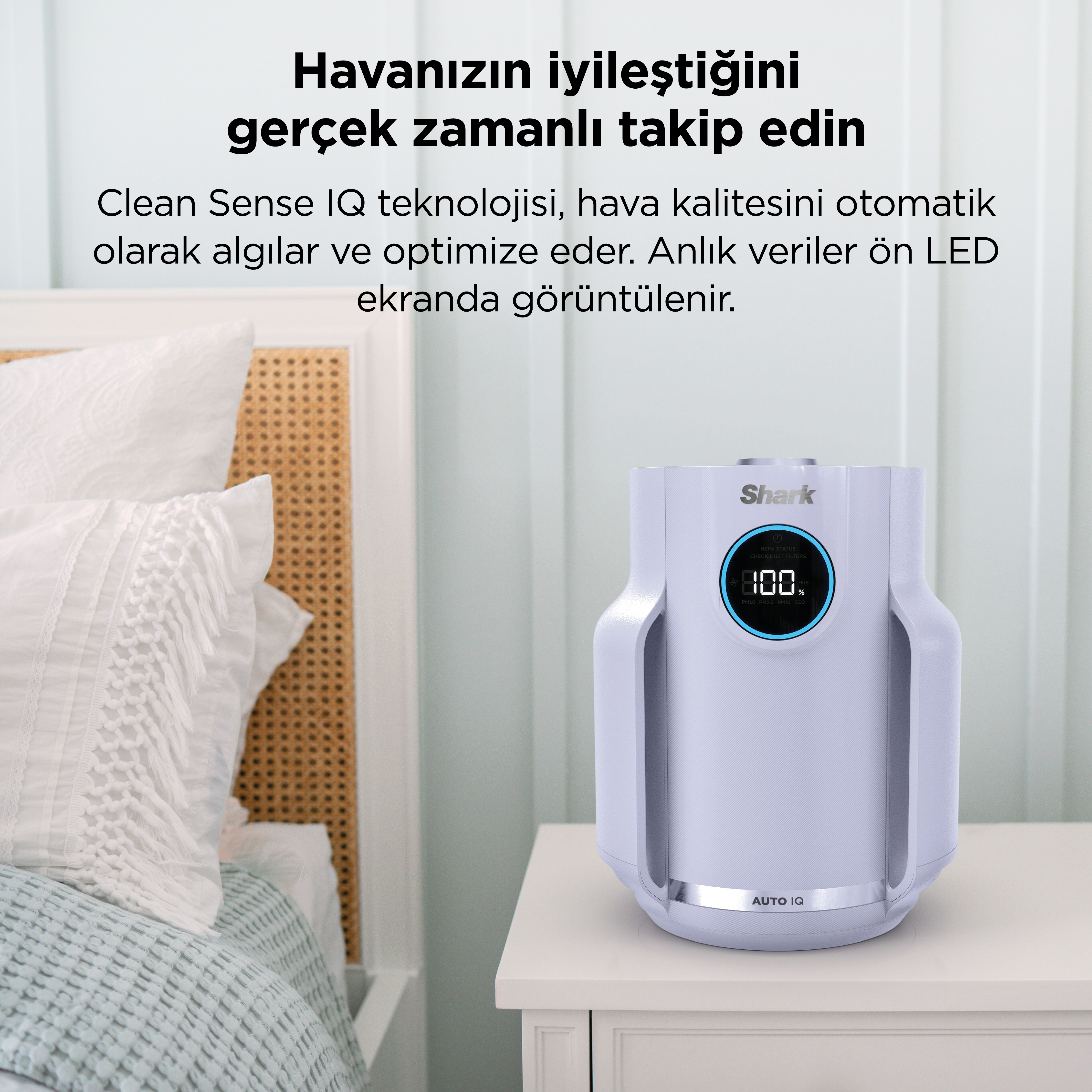 LED ekrana sahip beyaz bir hava temizleyici, yatağın yanındaki komodinin üzerinde duruyor.