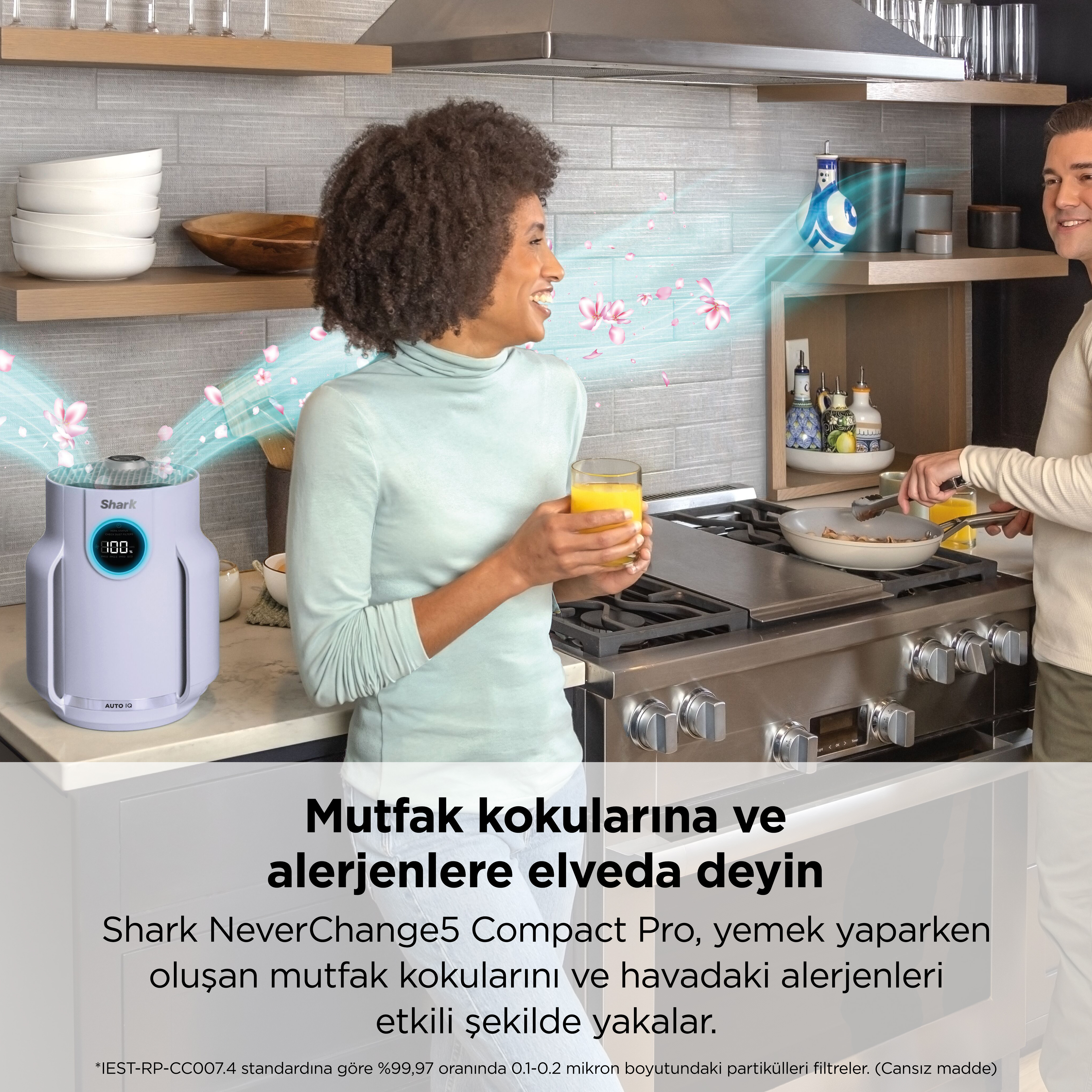 Bir kadın içerken, bir adam mutfakta yemek yapıyor.