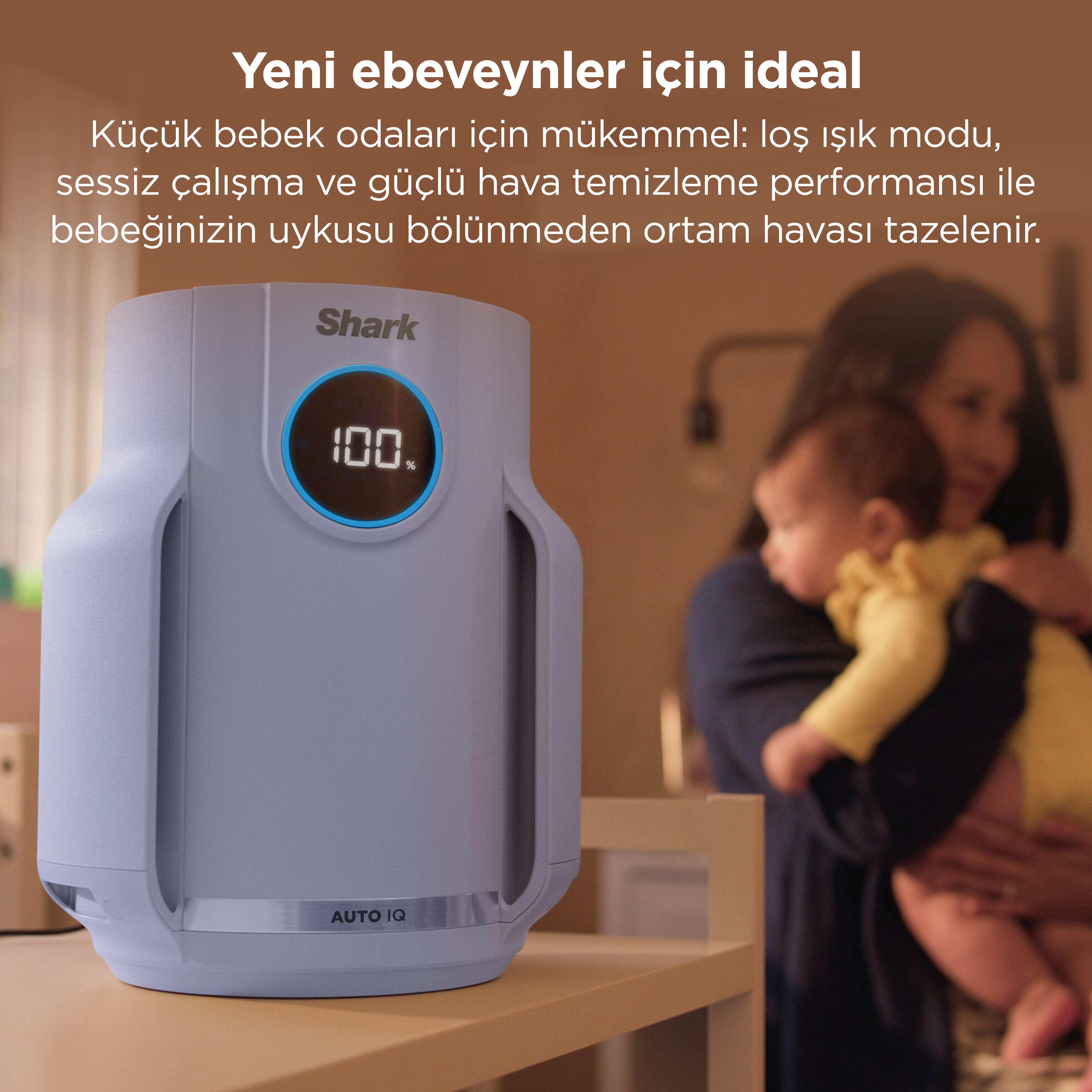 100% göstergeli açık gri bir hava temizleyici, bebek tutan bir annenin yanında duruyor.