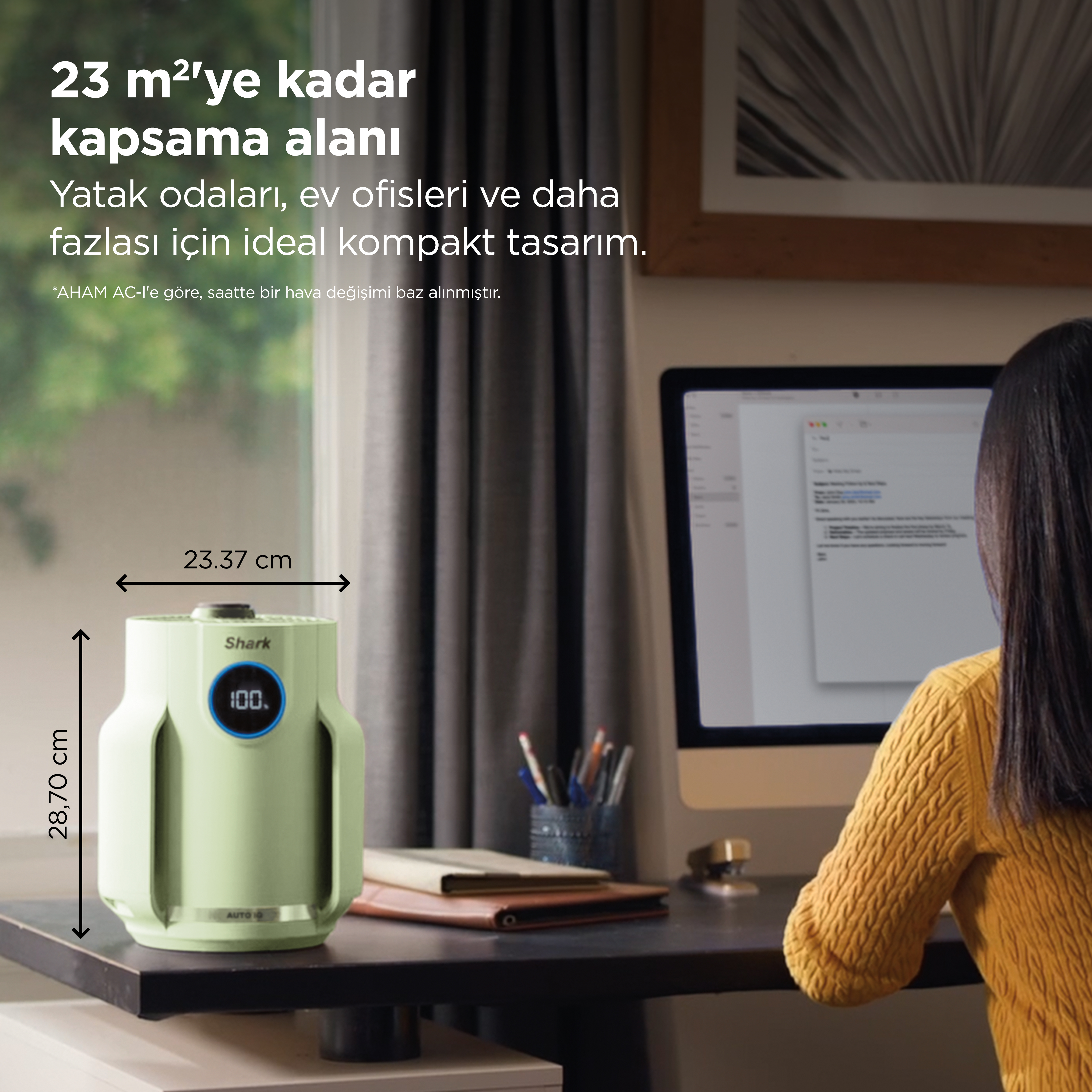 Yeşil bir hava temizleyici, bilgisayarın yanında masanın üzerinde duruyor.
