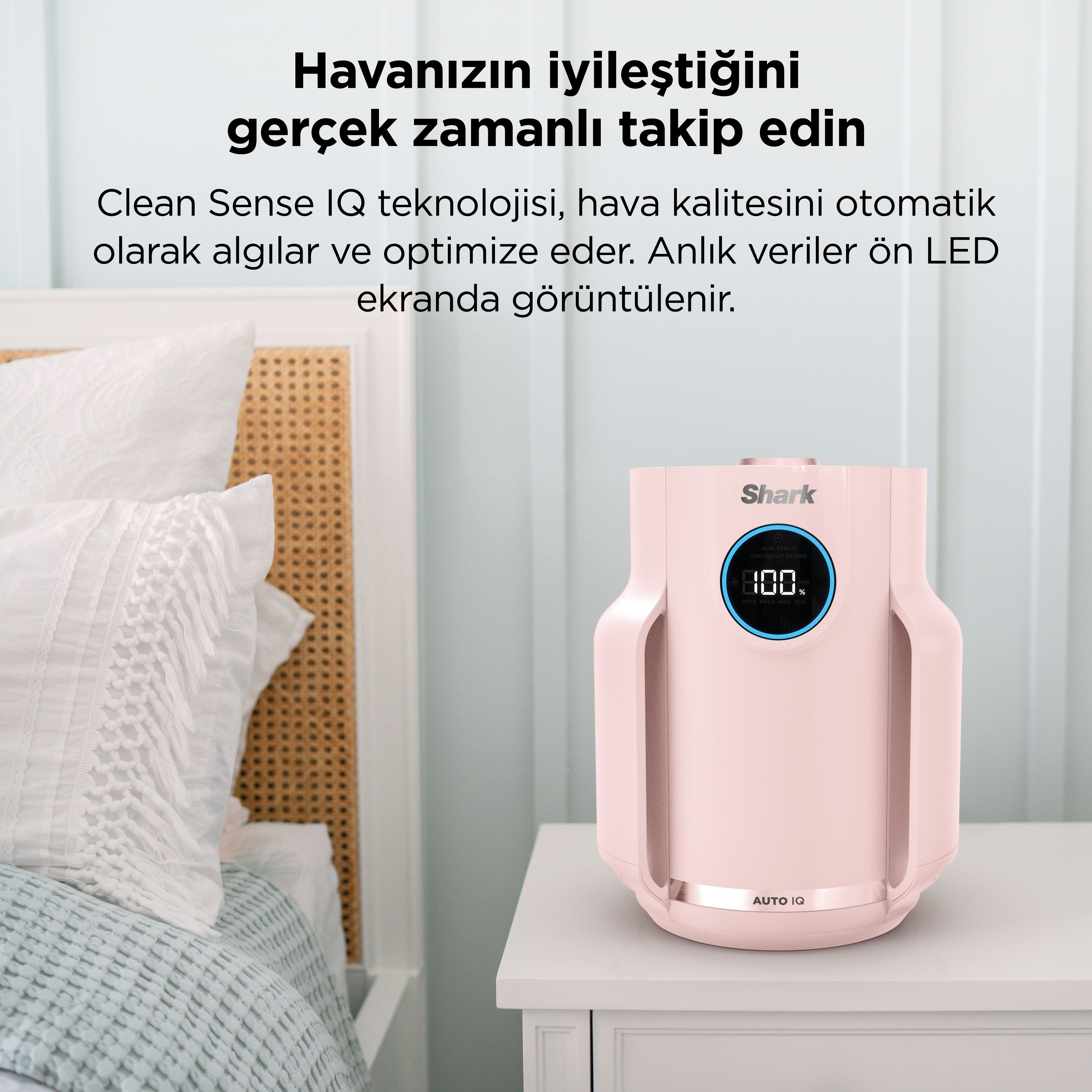 Pembe bir hava temizleyici, beyaz yastıklı bir yatağın yanındaki komodinin üzerinde duruyor.