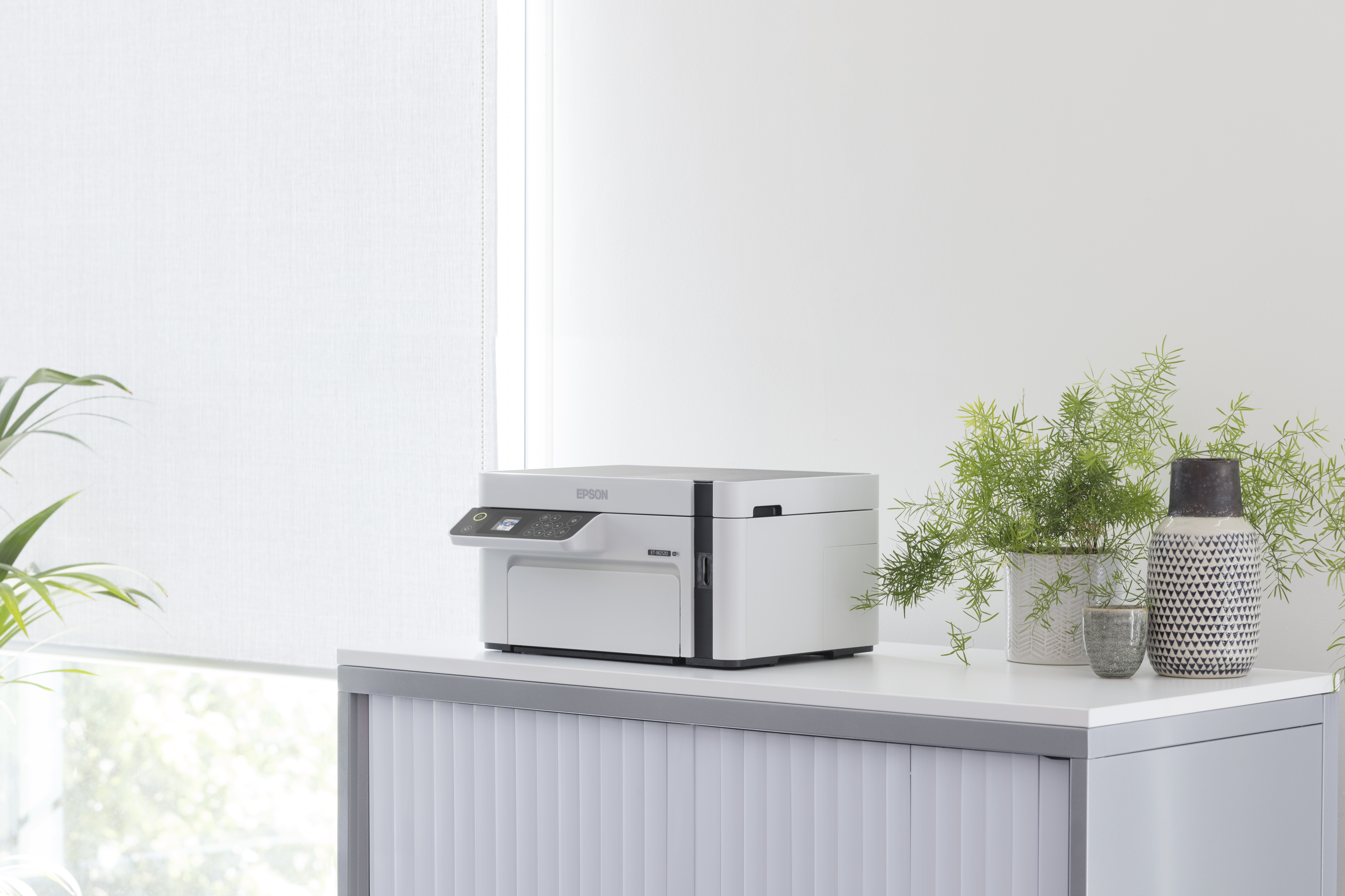 Ein weißer Epson Drucker steht auf einem weißen Schrank neben zwei Vasen und Pflanzen.