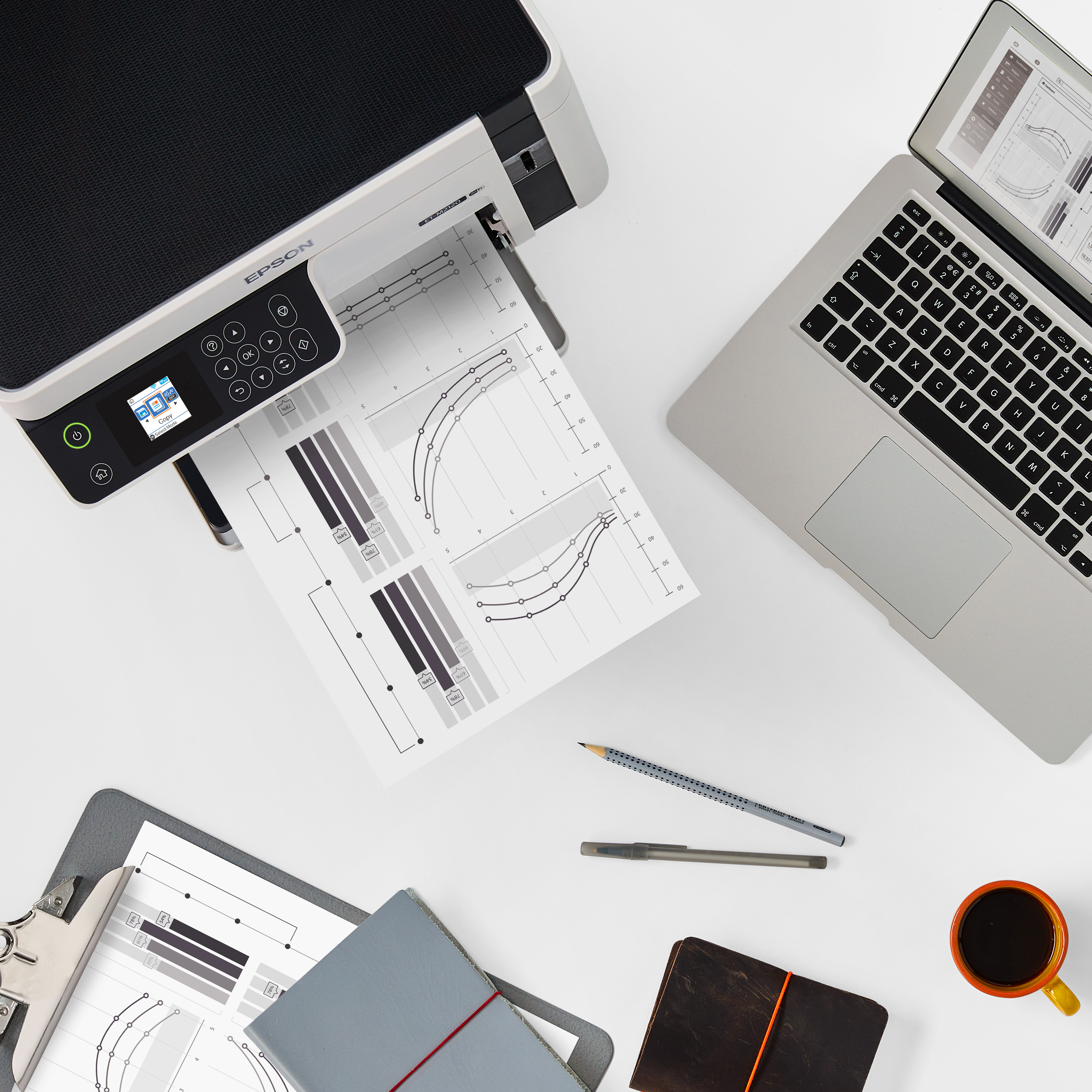 Ein Epson Drucker druckt Diagramme neben einem Laptop, Notizbüchern und Kaffee.