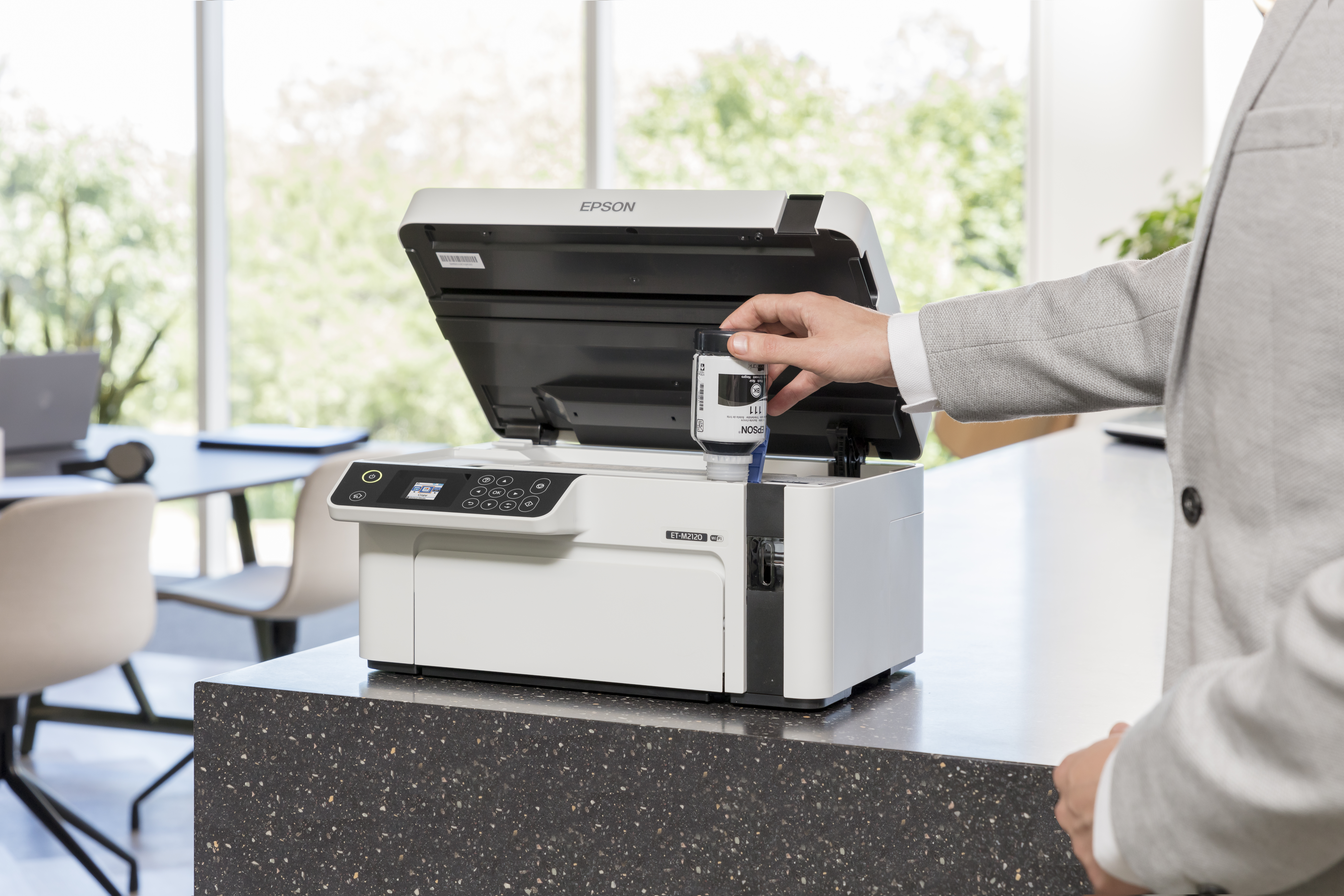 Mann füllt Tinte in einen weißen Epson Drucker auf einem Schreibtisch.