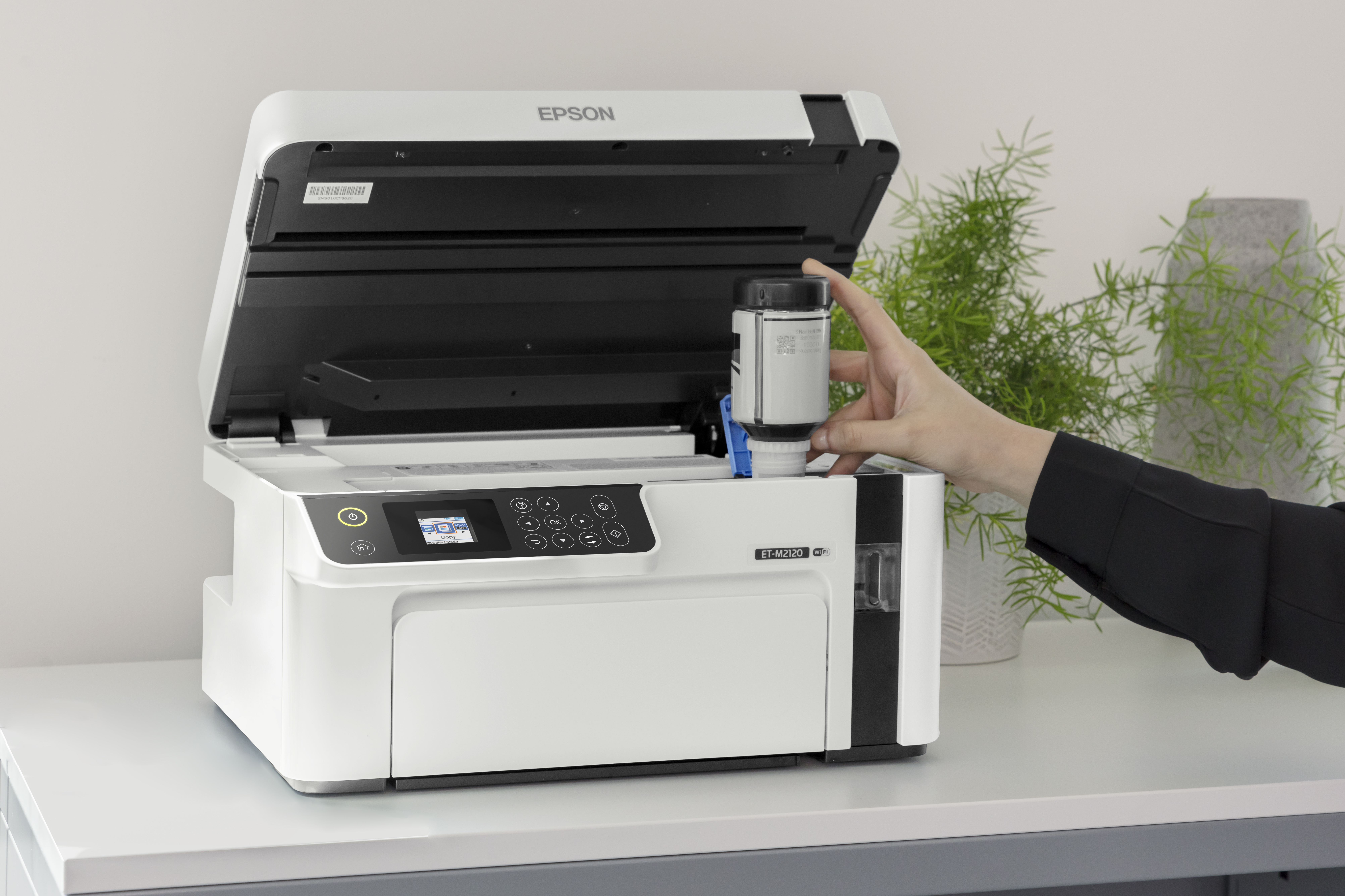 Eine Hand füllt Tinte in einen weißen Epson Drucker, der auf einem Schreibtisch steht.