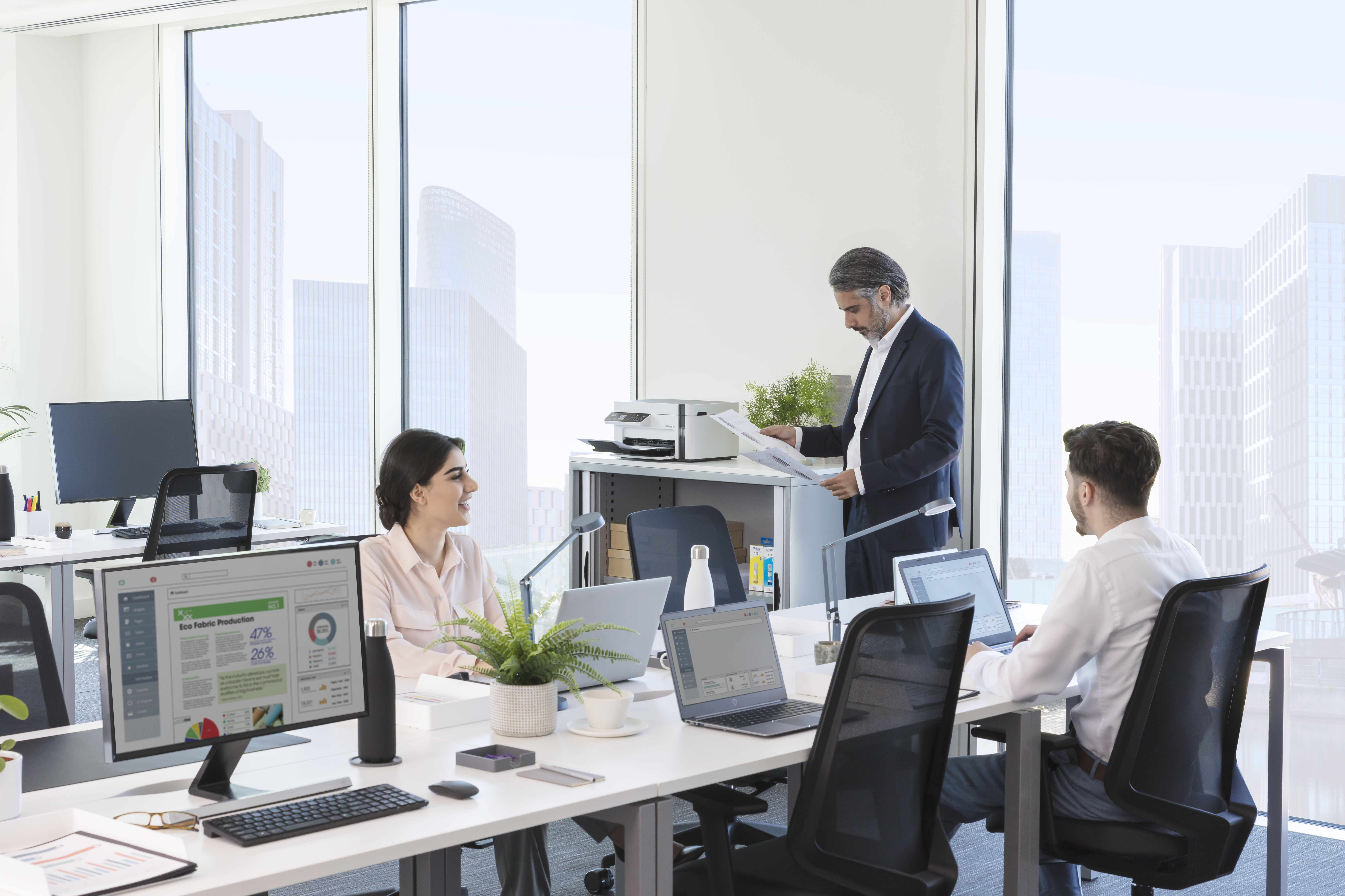 Büro mit drei Personen, die an Schreibtischen arbeiten, mit Blick auf die Stadt.