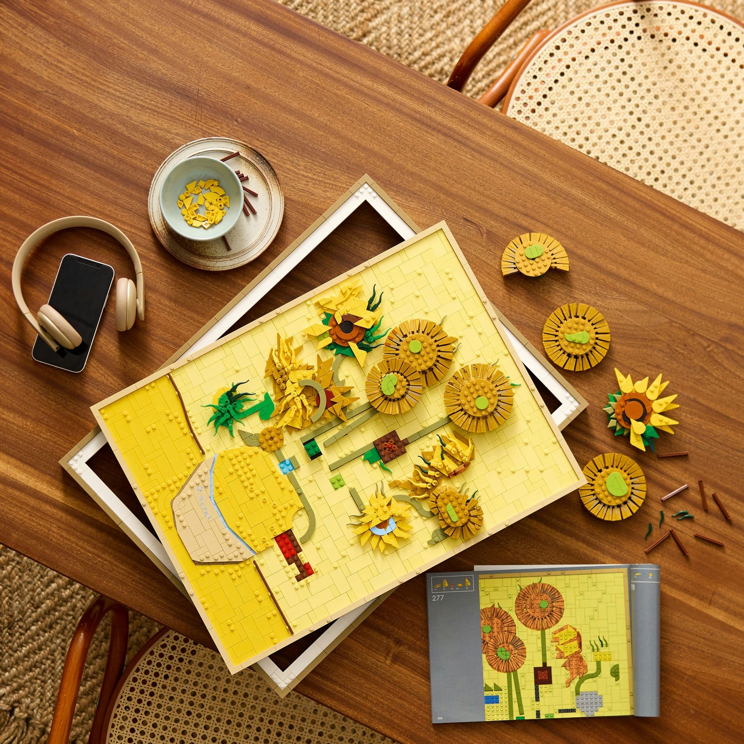 Set di girasoli LEGO in costruzione su tavolo di legno con cuffie e telefono.