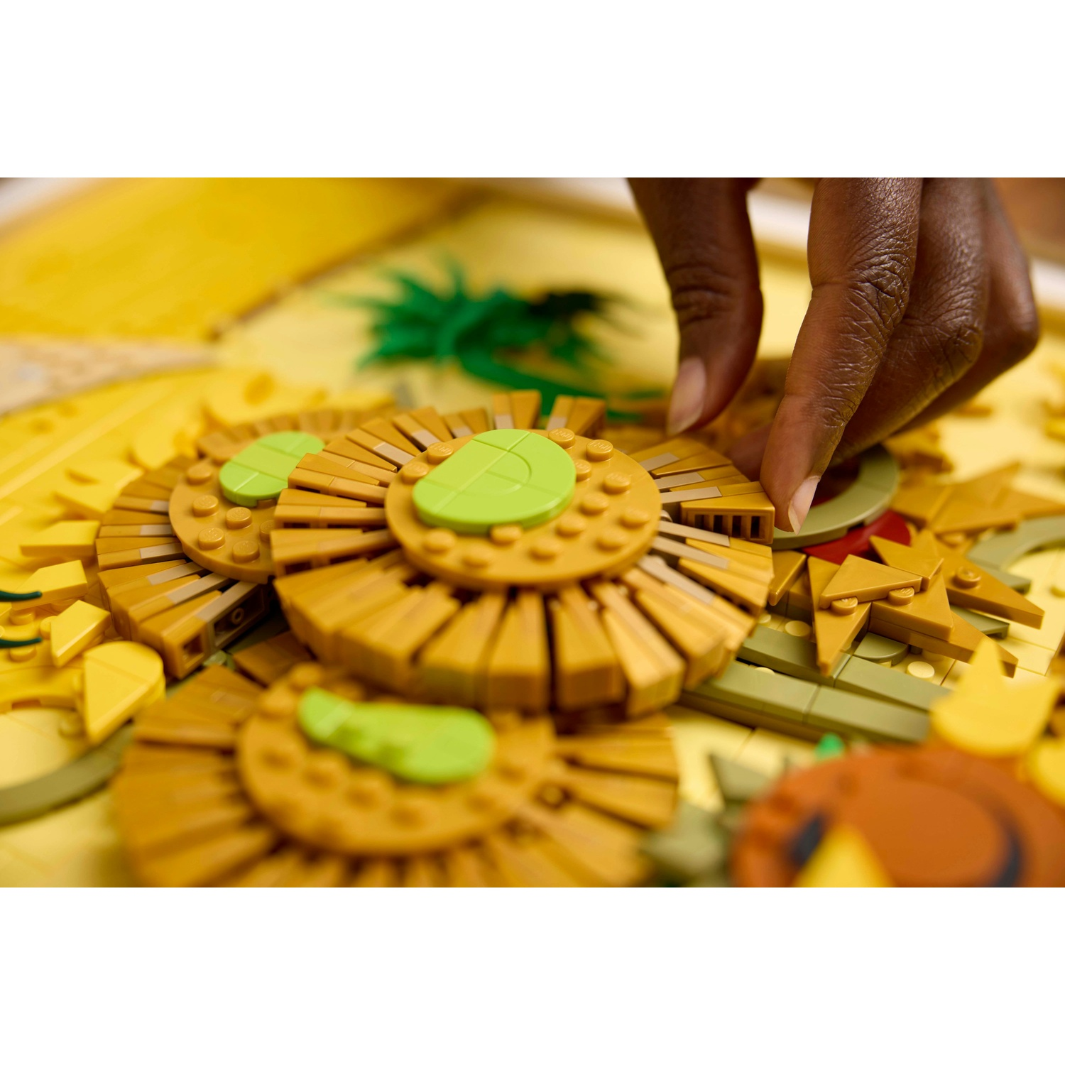 Una mano sta costruendo un fiore Lego giallo con accenti verdi.