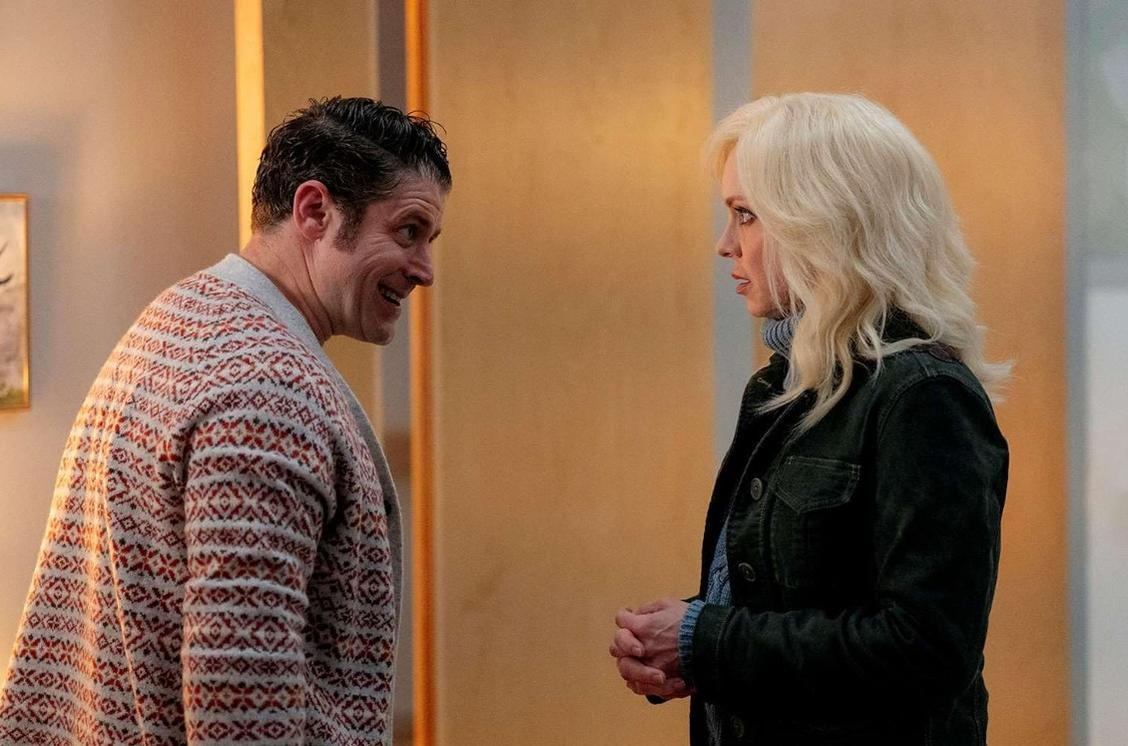 Mann mit gemustertem Pullover spricht mit Frau mit blonden Haaren in dunkler Jacke.