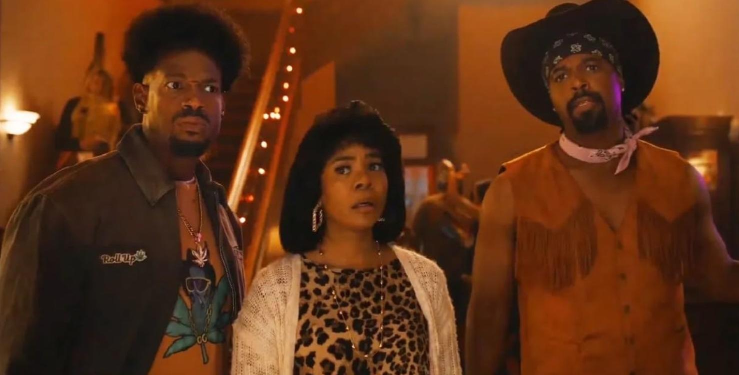 Drei Personen stehen nebeneinander. Ein Mann mit Afro, eine Frau mit Leo-Muster und ein Mann mit Cowboyhut.