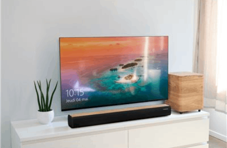 Un televisor de pantalla plana muestra una escena de paisaje, con un subwoofer de madera y barra de sonido.