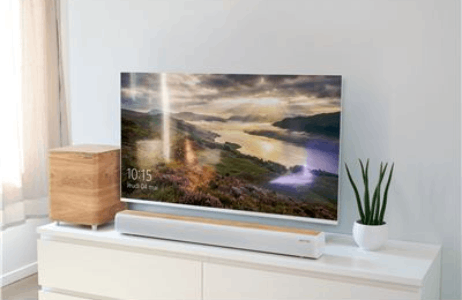 Una sala de estar moderna con TV, caja de madera, barra de sonido y planta en un mueble blanco.