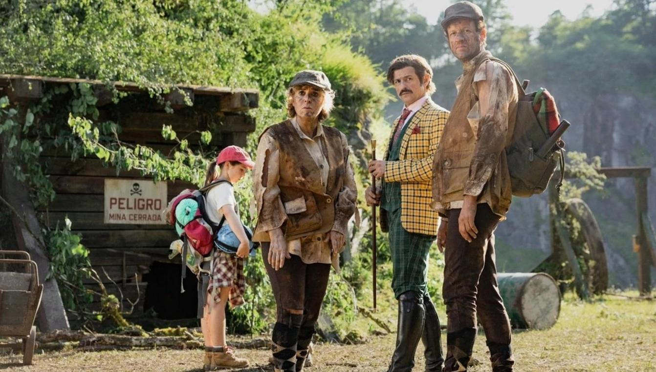 Vier schmutzige Abenteurer stehen vor einer Holzhütte mit einem Warnschild.