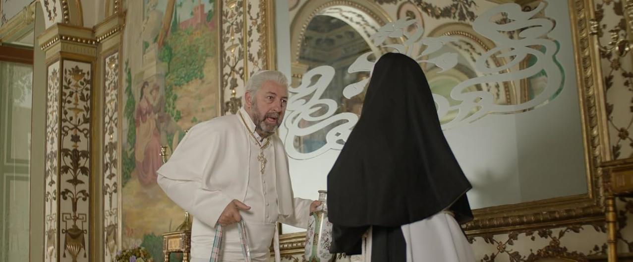 Ein Mann in weißer Kleidung spricht mit einer Nonne in schwarzer Kleidung.