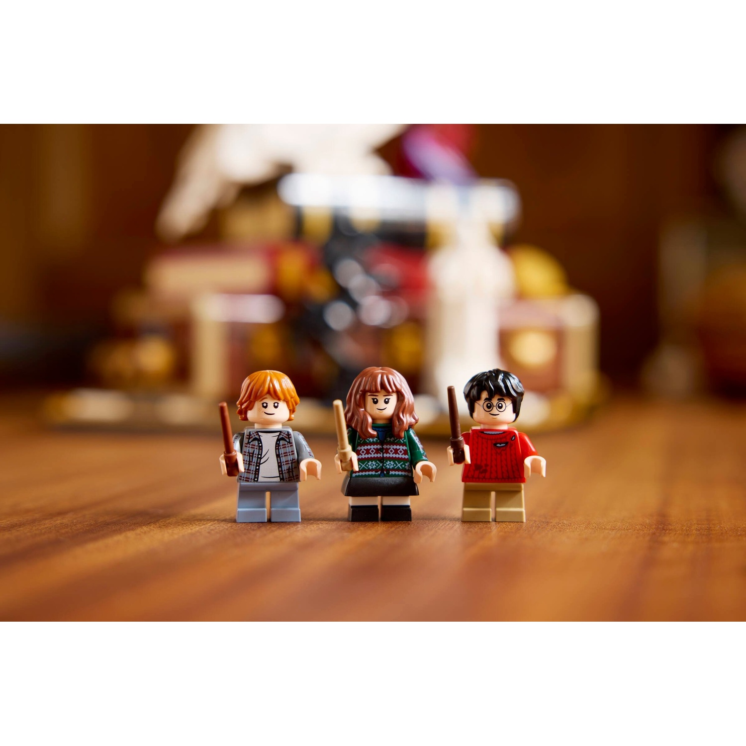 Tre minifigure Lego: Ron, Hermione e Harry, in piedi sul legno.
