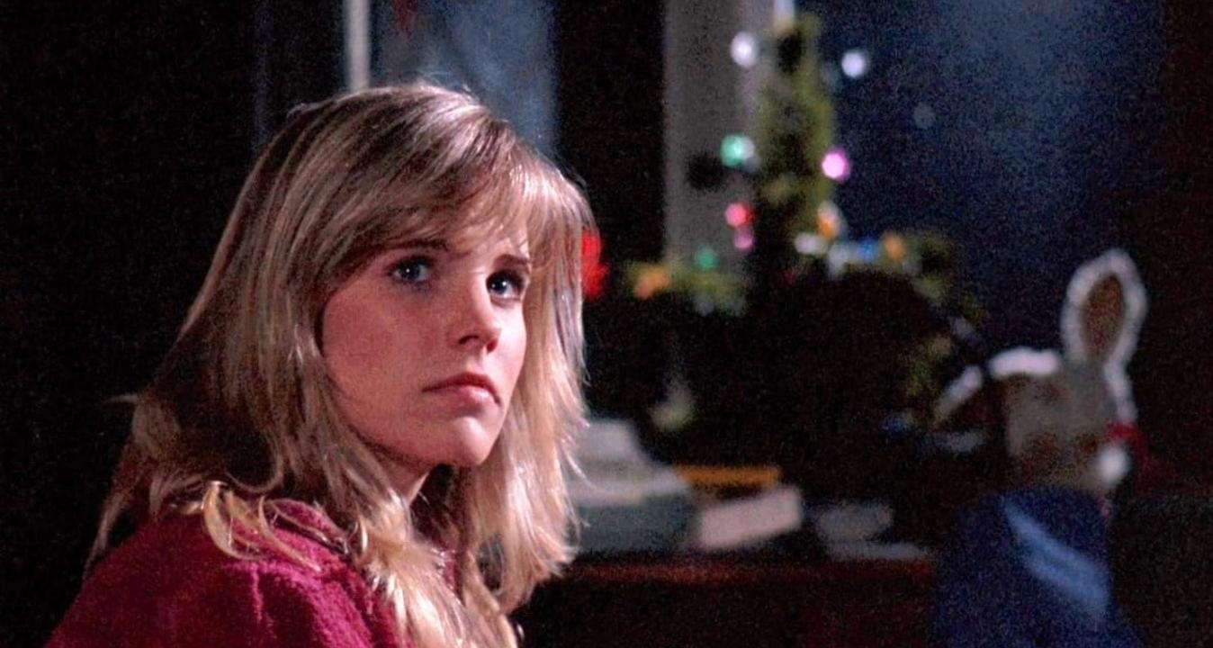 Junge Frau mit blonden Haaren blickt nach links, im Hintergrund ein Weihnachtsbaum mit Lichtern.