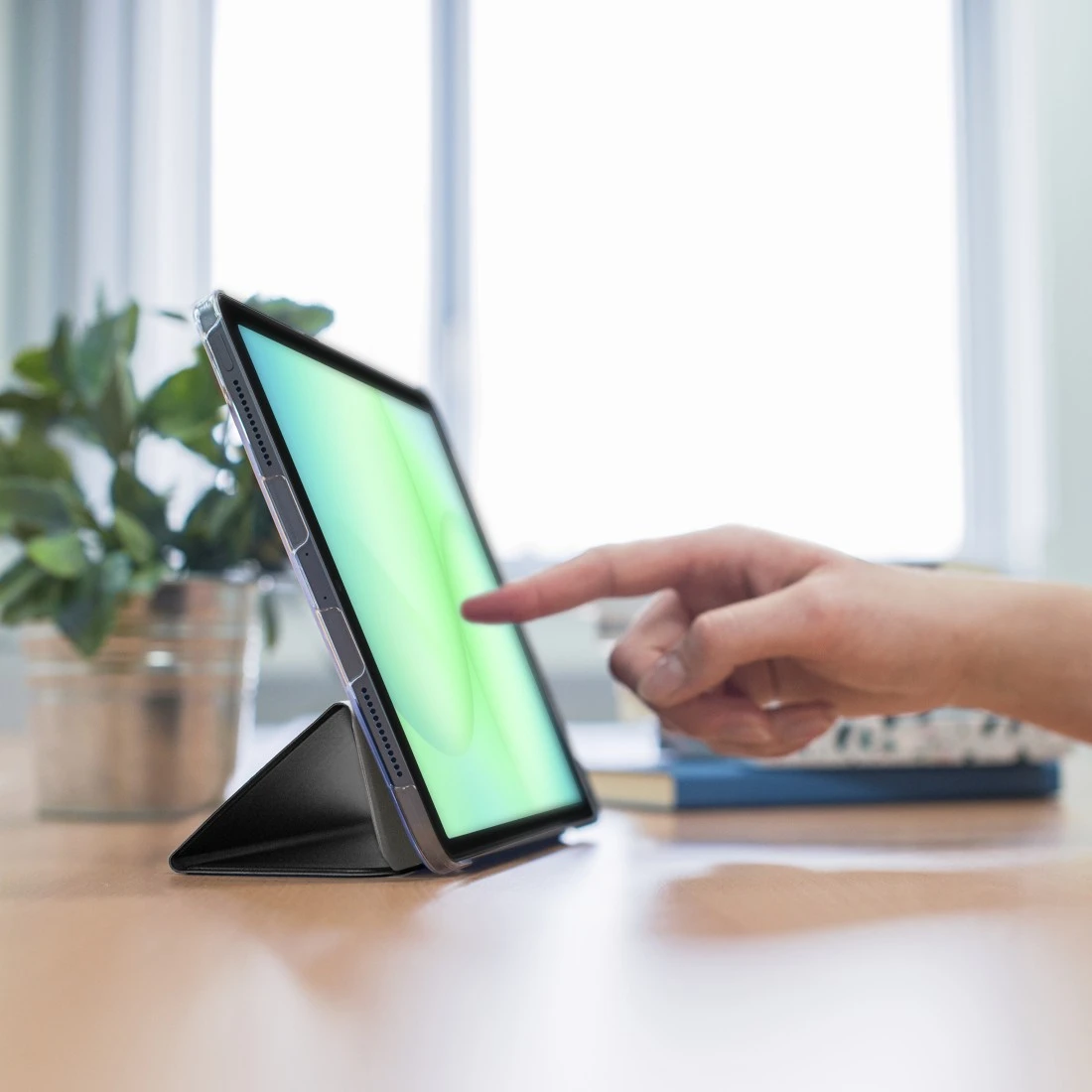 Ein Finger tippt auf einen Tablet-Bildschirm mit grünem Hintergrund, daneben eine Pflanze.