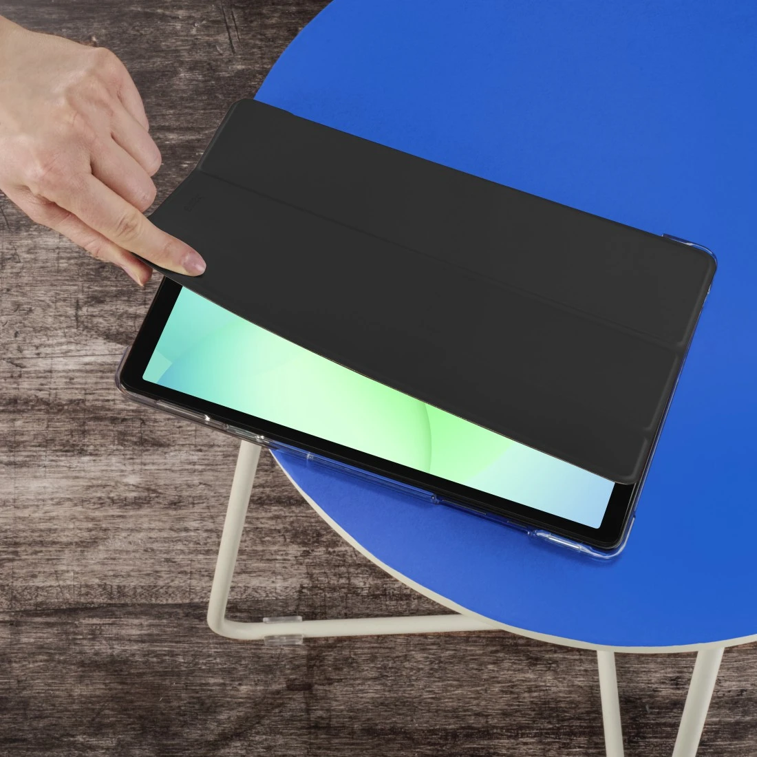 Eine Hand öffnet eine schwarze Tablet-Hülle auf einem blauen Tisch.