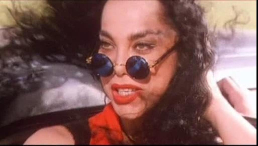 Frau mit Sonnenbrille und rotem Lippenstift im Auto, Wind in den Haaren.
