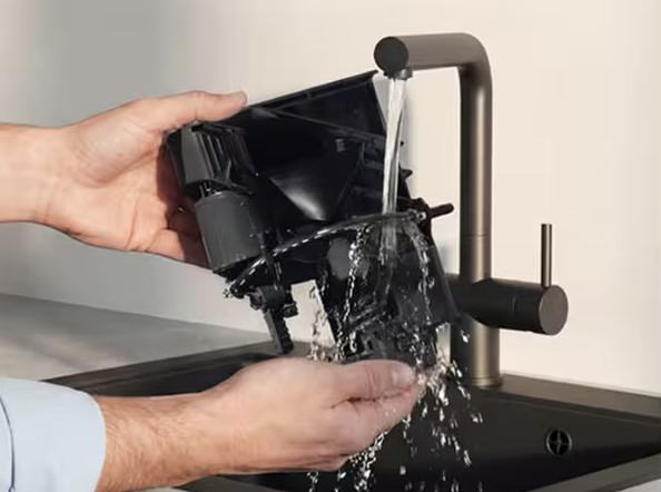 Ręce płuczą czarną plastikową część pod bieżącą wodą z kranu.