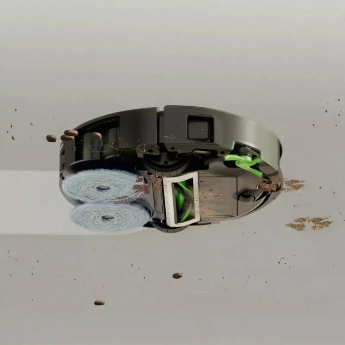 Robot sprzątający z dwoma niebieskimi szczotkami czyści brud i ziarna kawy.