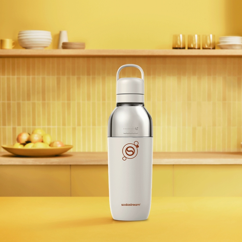Biała butelka Sodastream z srebrną górą stoi na żółtym stole.