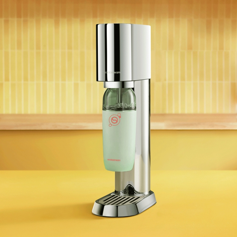 Srebrne urządzenie SodaStream z zieloną butelką na żółtej powierzchni.