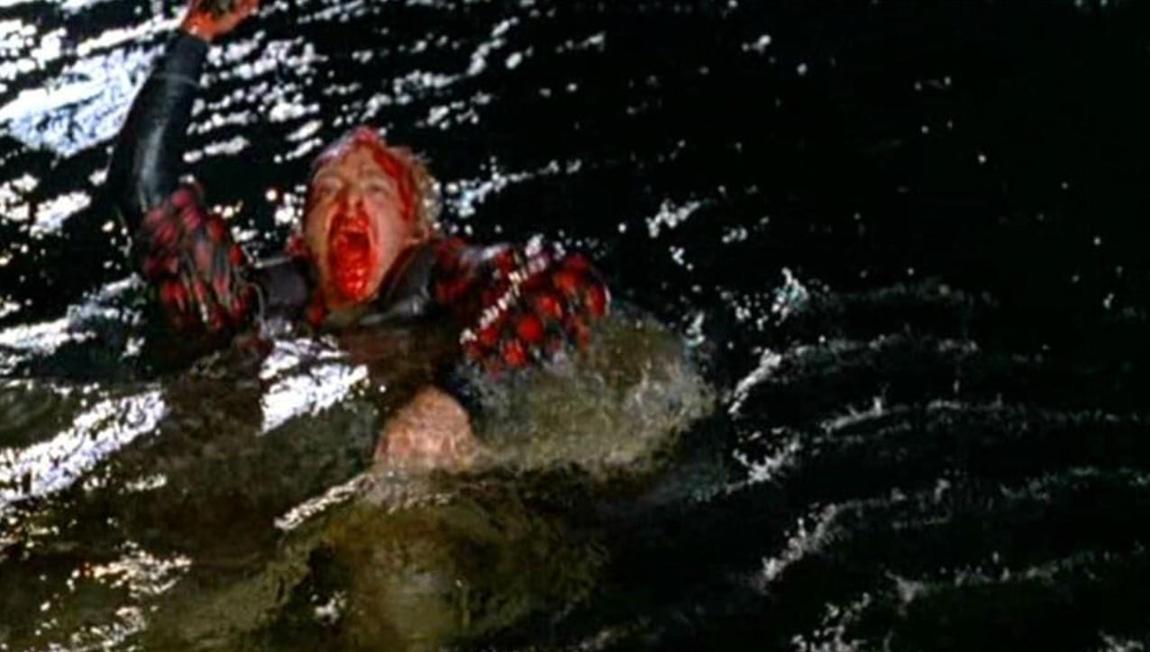 Eine blutende Person mit roten Handschuhen kämpft im dunklen Wasser.